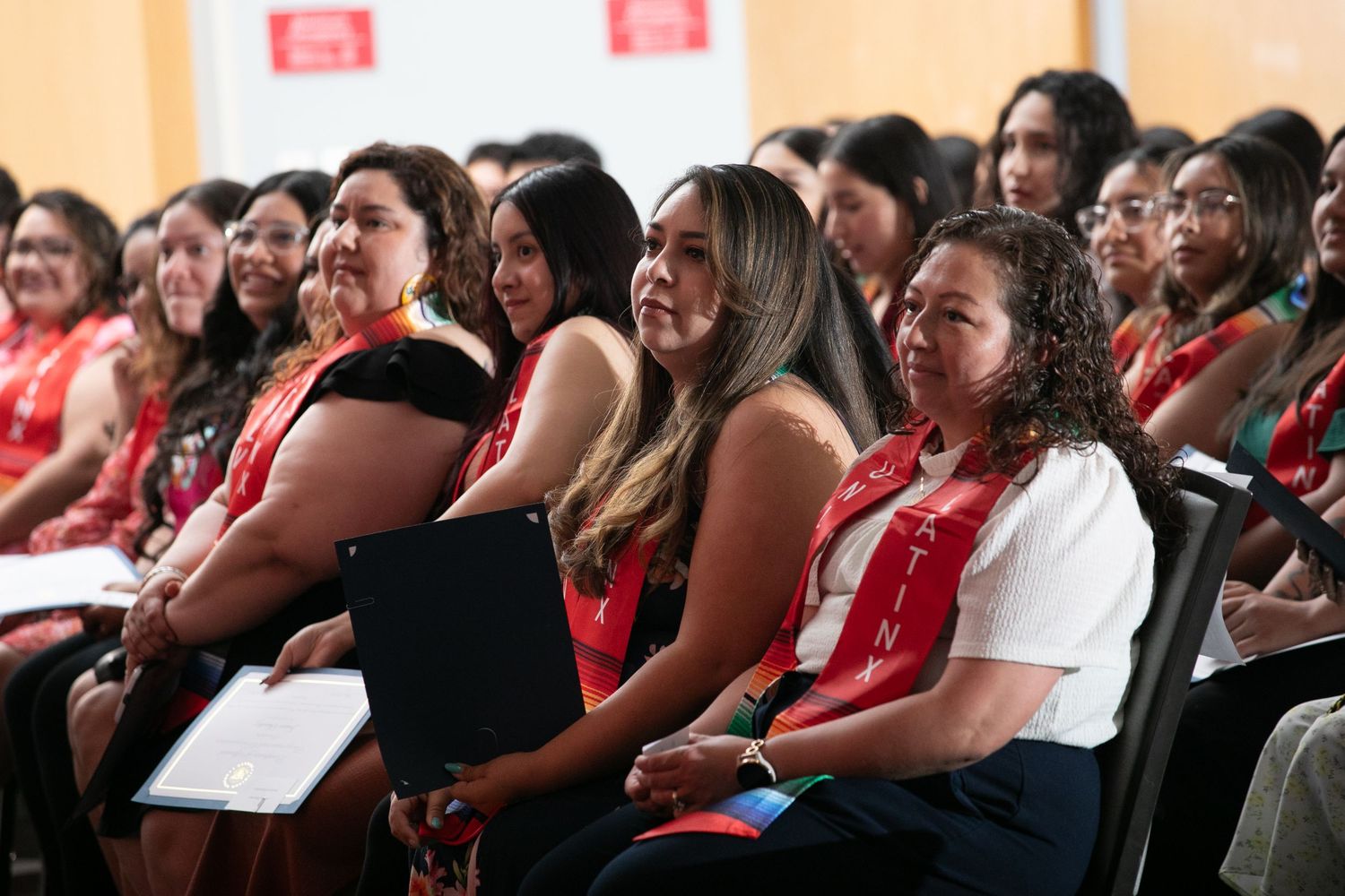 An engaged audience wearing red shirts laughs and smiles while seated in an auditorium during an event.