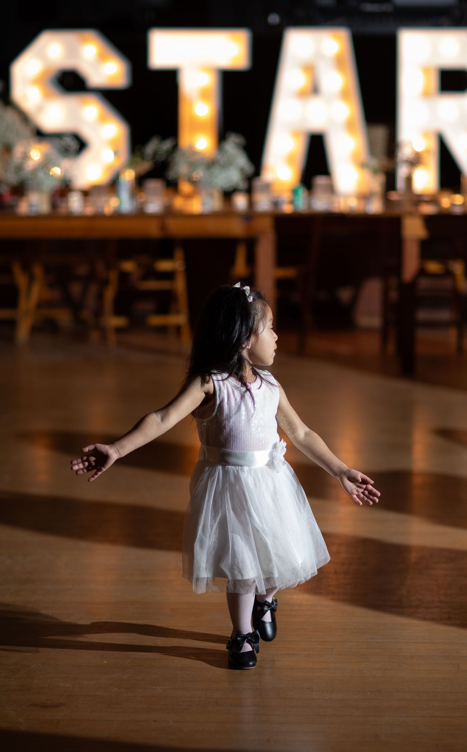 A young dancer in a white tulle dress twirls in front of illuminated marquee letters.