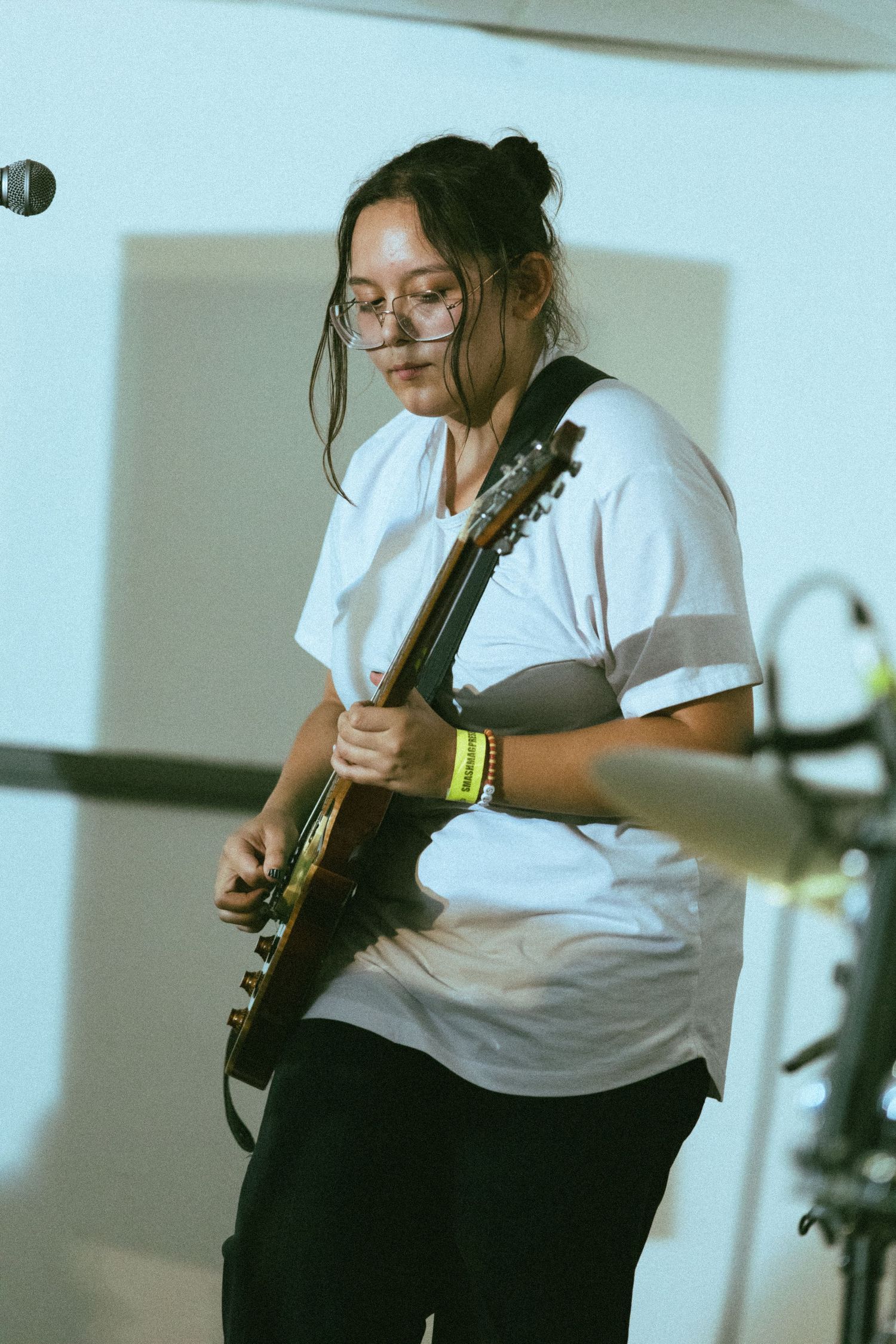 Guitar player in white t-shirt performs during an indoor concert set.
