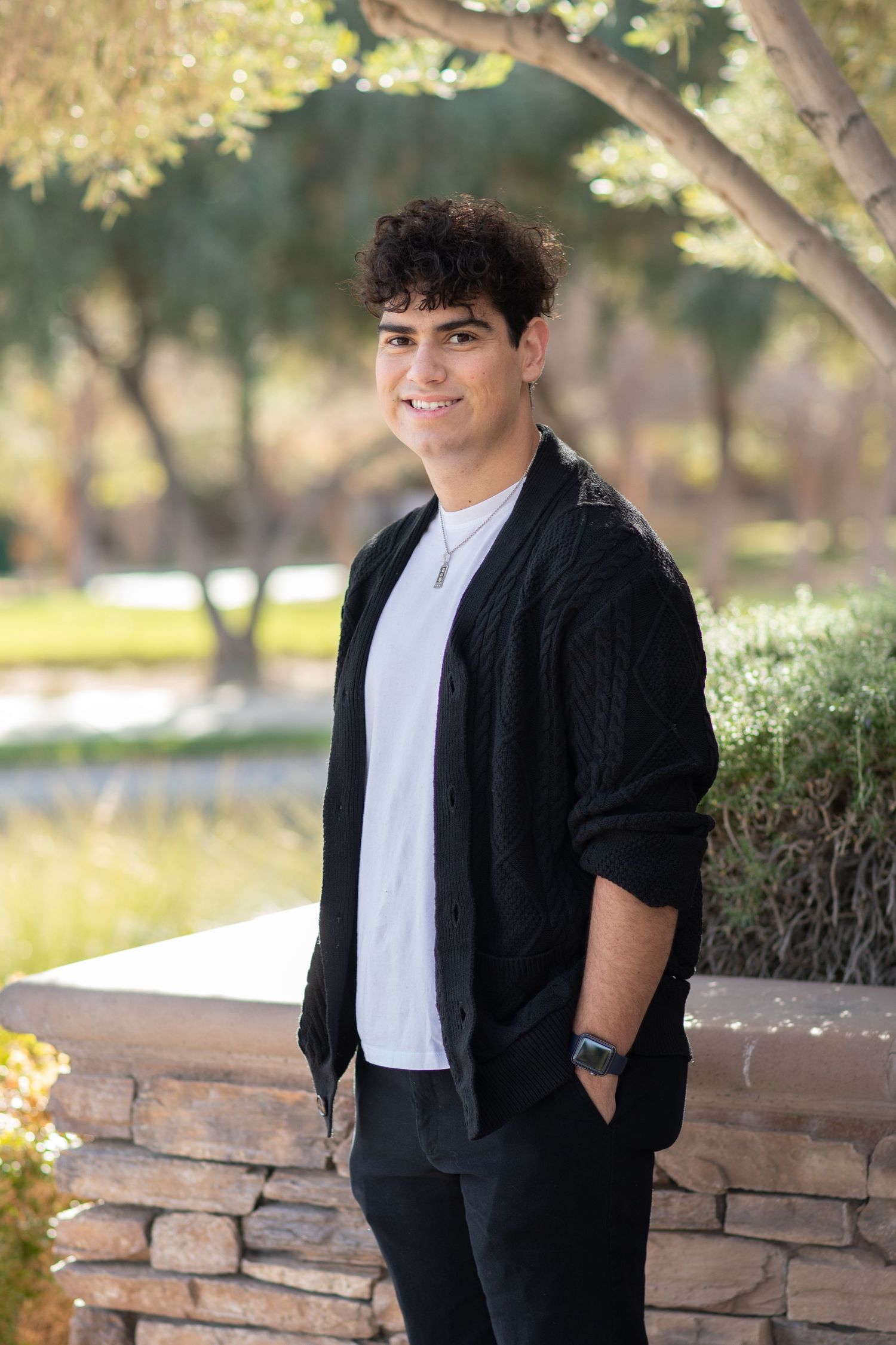 Young person in casual black outfit poses against garden background with natural lighting.