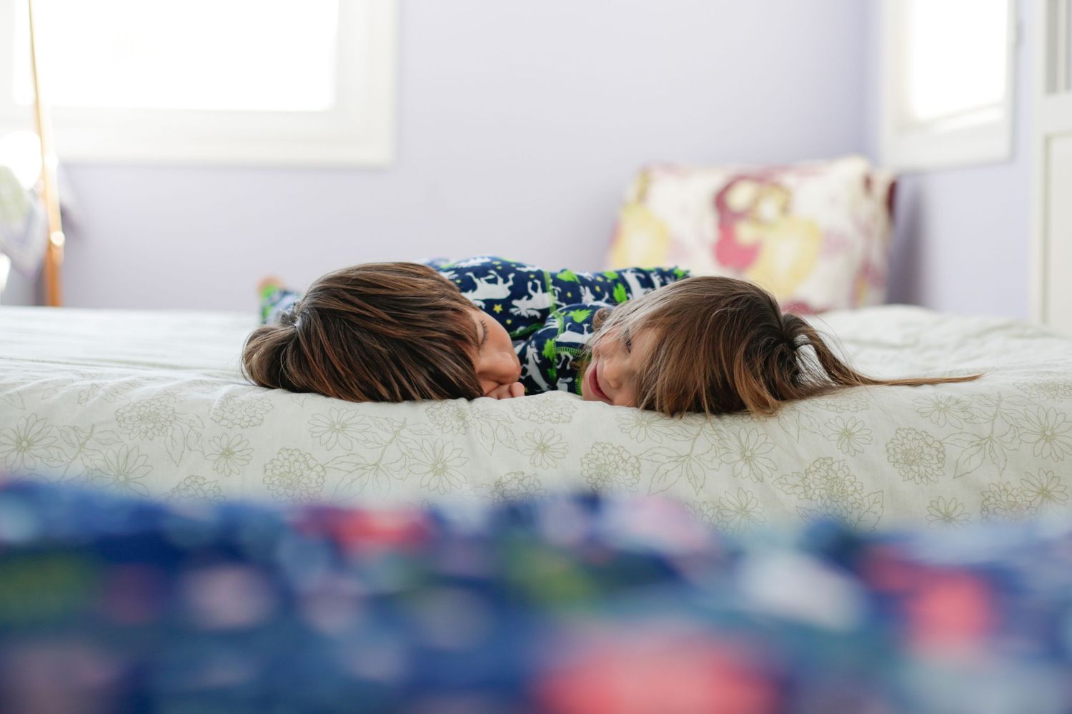 Two kids lying face down on a bed wearing matching pajamas.
