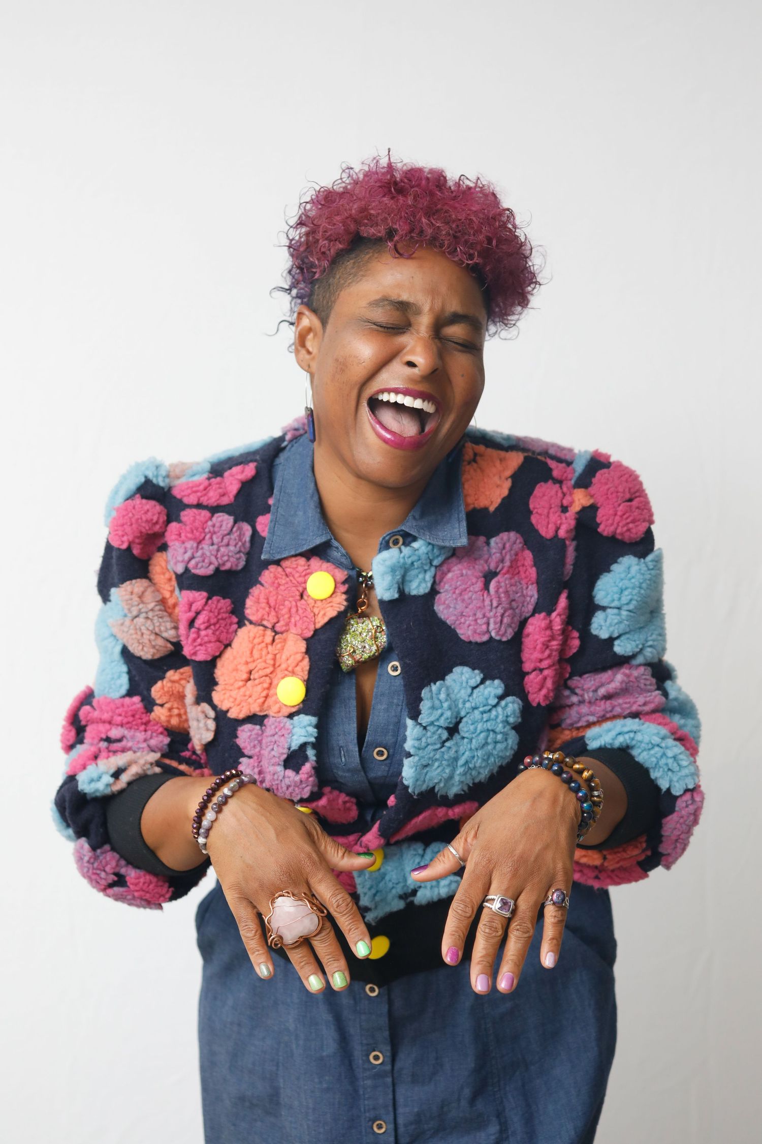 Woman wearing colorful floral jacket laughs joyfully against white background.