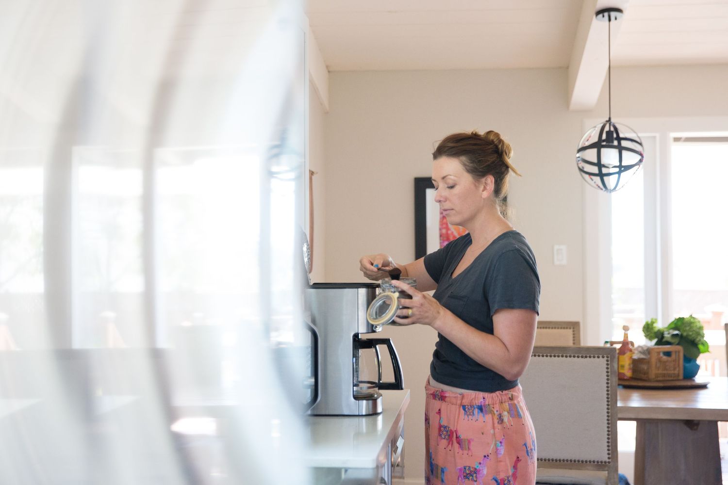 Woman in casual attire checking phone while standing in modern kitchen.