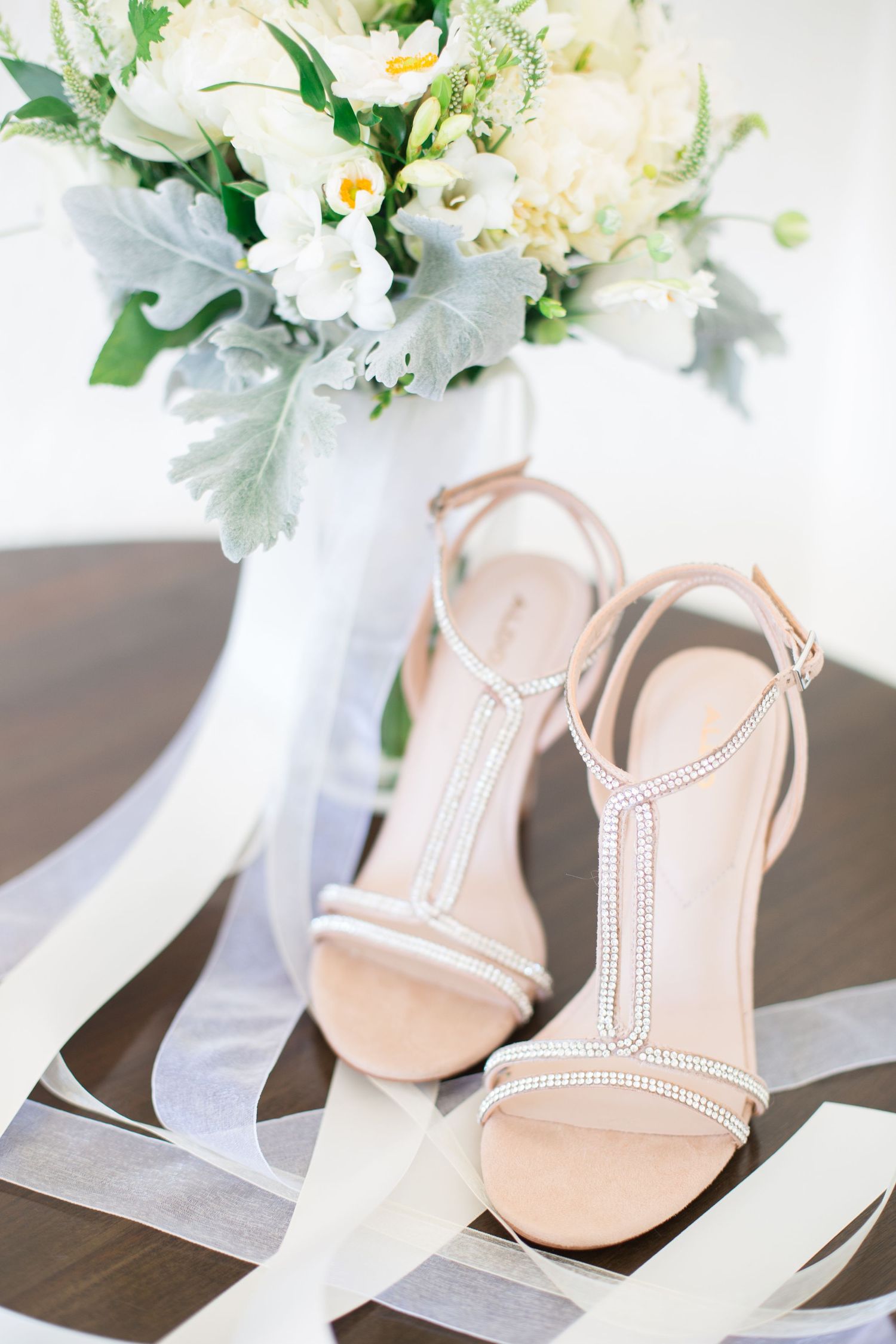 Nude wedding sandals with crystal details displayed next to a white floral arrangement.