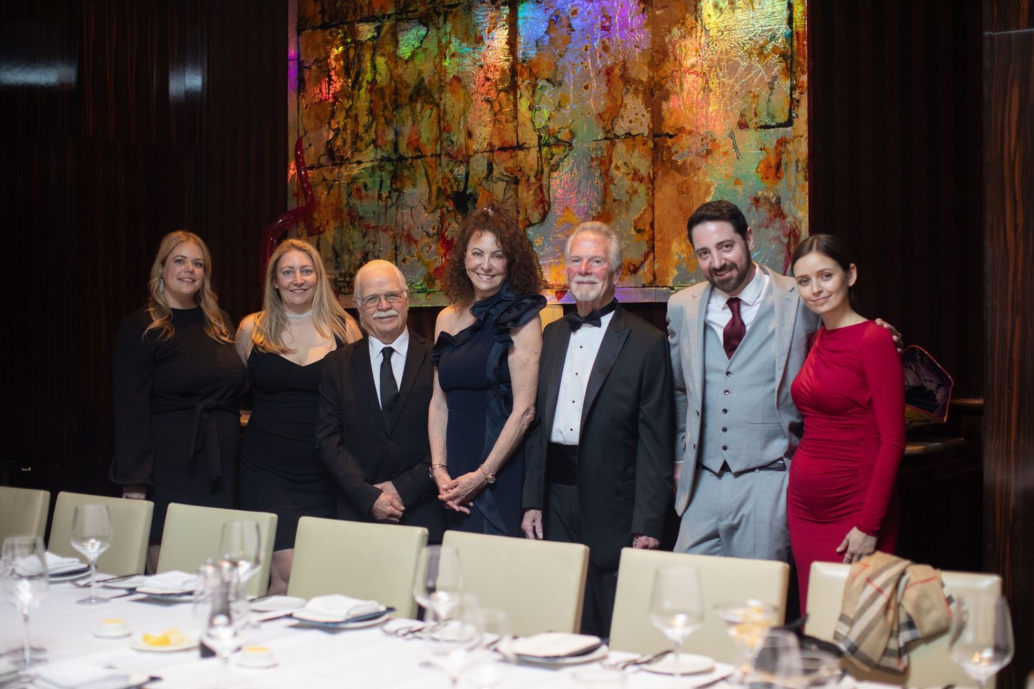 People gathered around dinner tables at an elegant celebration with warm lighting and formal attire.