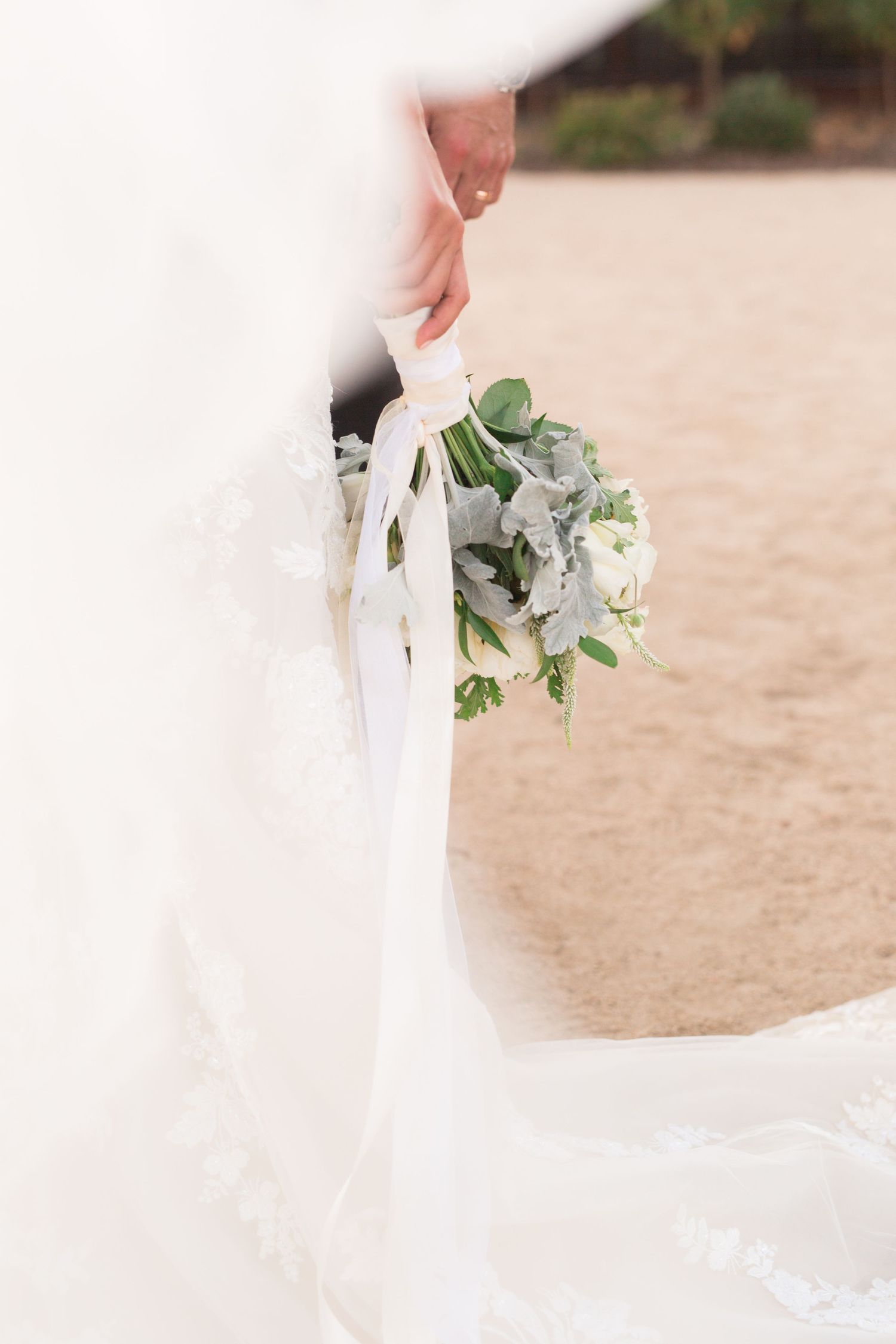 White and green bridal bouquet held against flowing wedding dress and veil.