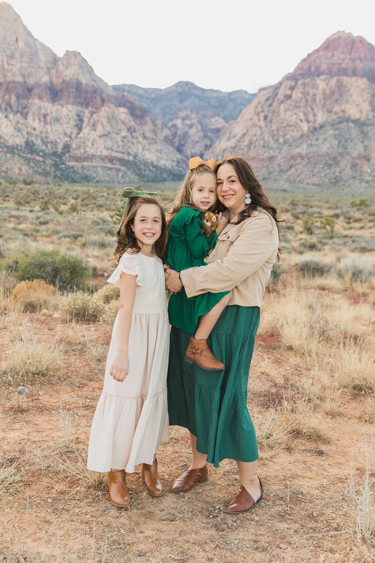Three people in coordinated green and beige outfits pose together against red rock mountains.