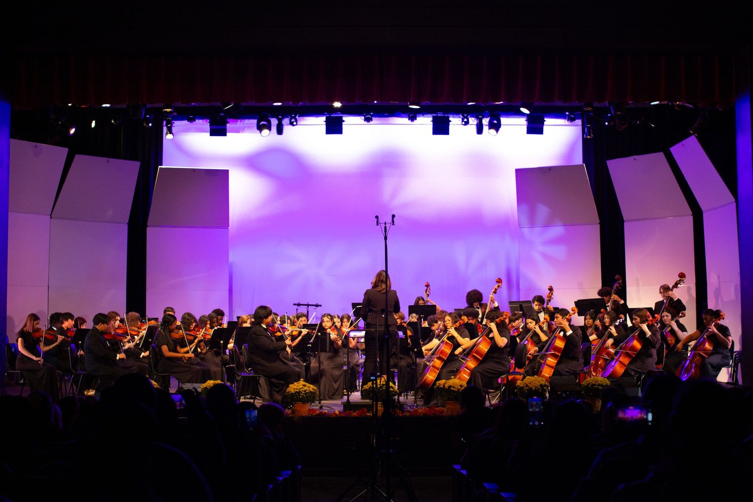 Full orchestra on stage with purple lighting and curved architectural elements.