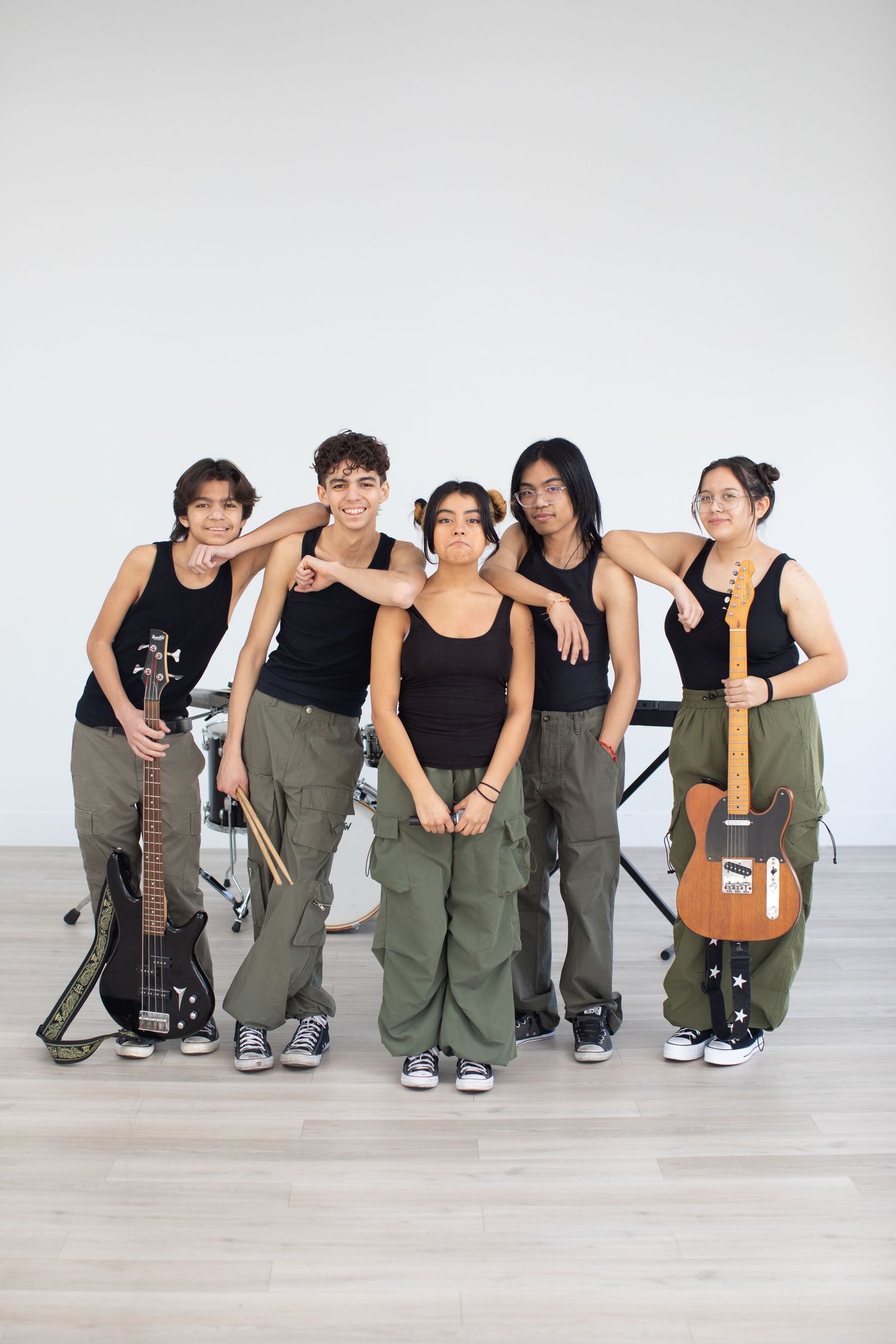 Music group in matching black tanks and cargo pants poses with their instruments.