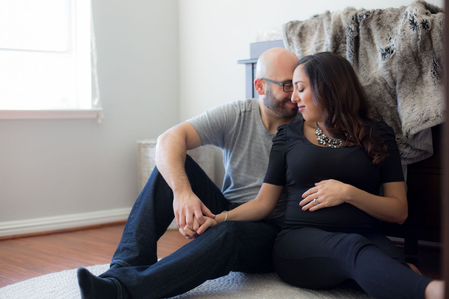 Couple sits together on floor against wall in casual attire.