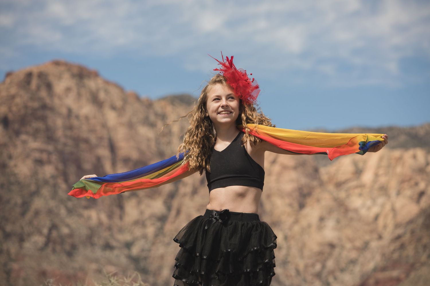 Dancer with rainbow scarf performs against red rock canyon landscape.