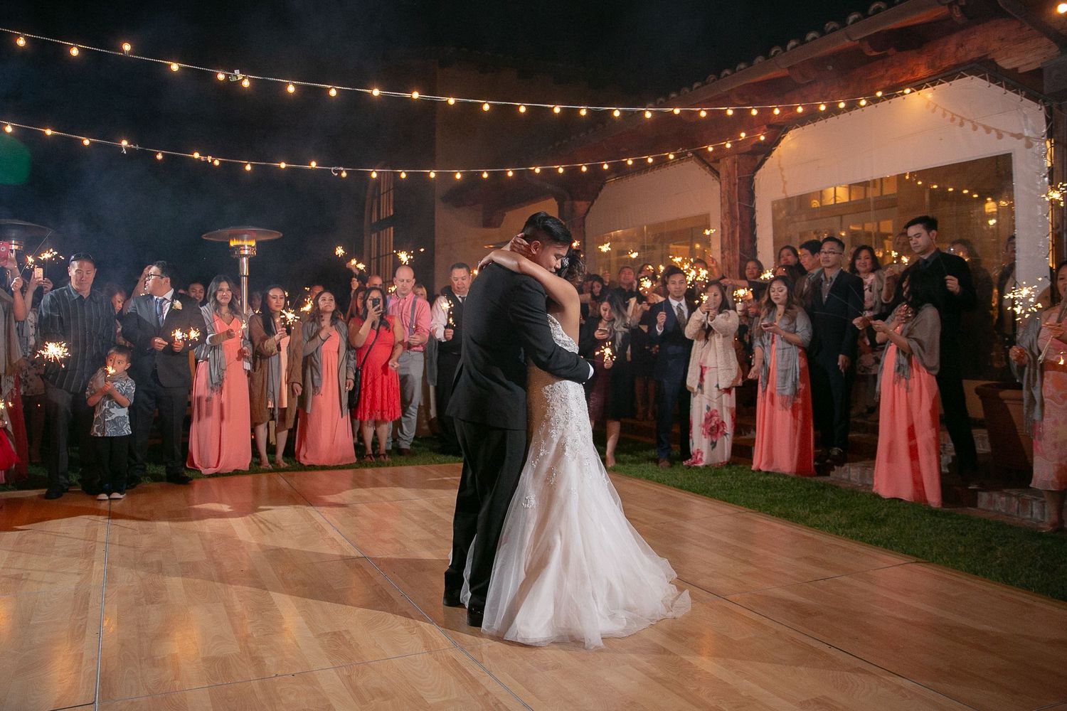 Couples dancing outdoors at night under romantic string lights at an elegant wedding reception.