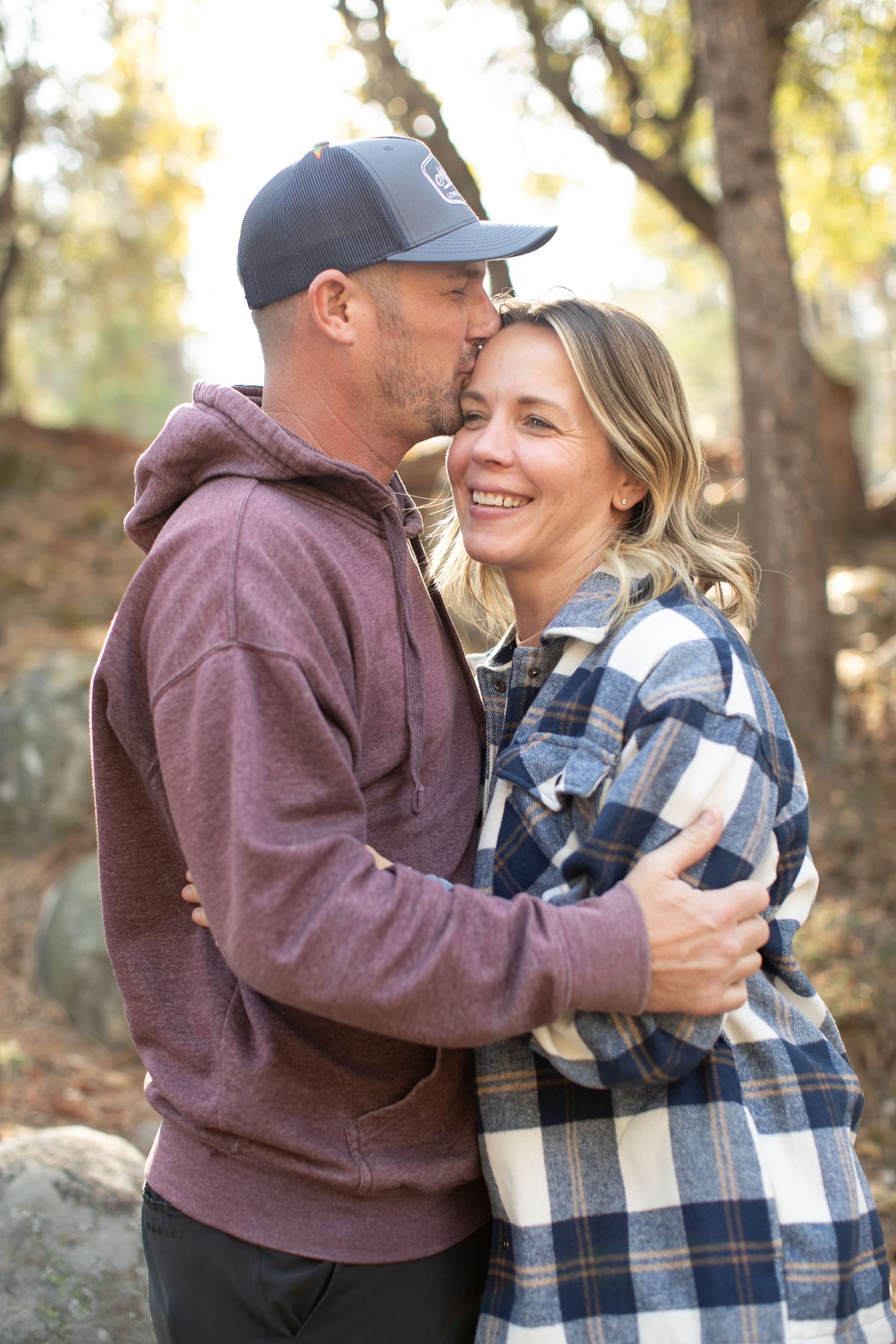 Autumn engagement photos show a couple embracing while wearing casual burgundy and plaid outfits.