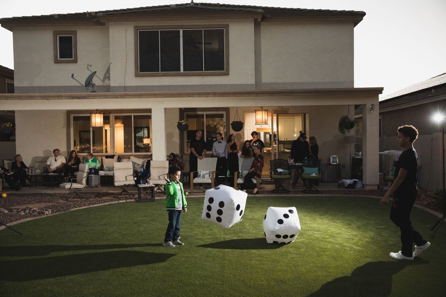 Outdoor party scene with giant inflatable dice on a lawn under evening lights.