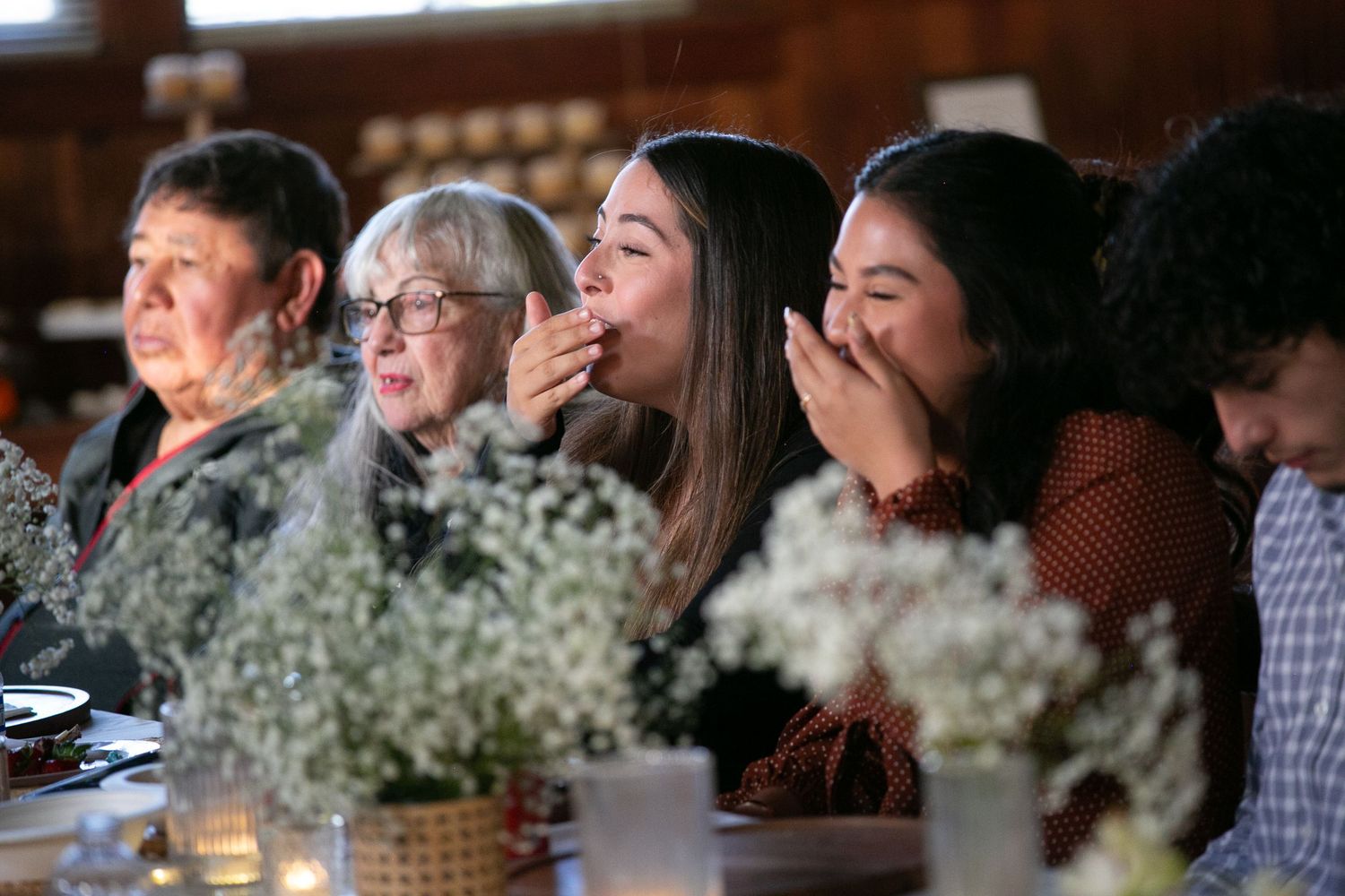 Guests react emotionally during a celebration with baby's breath floral centerpieces on dining tables.
