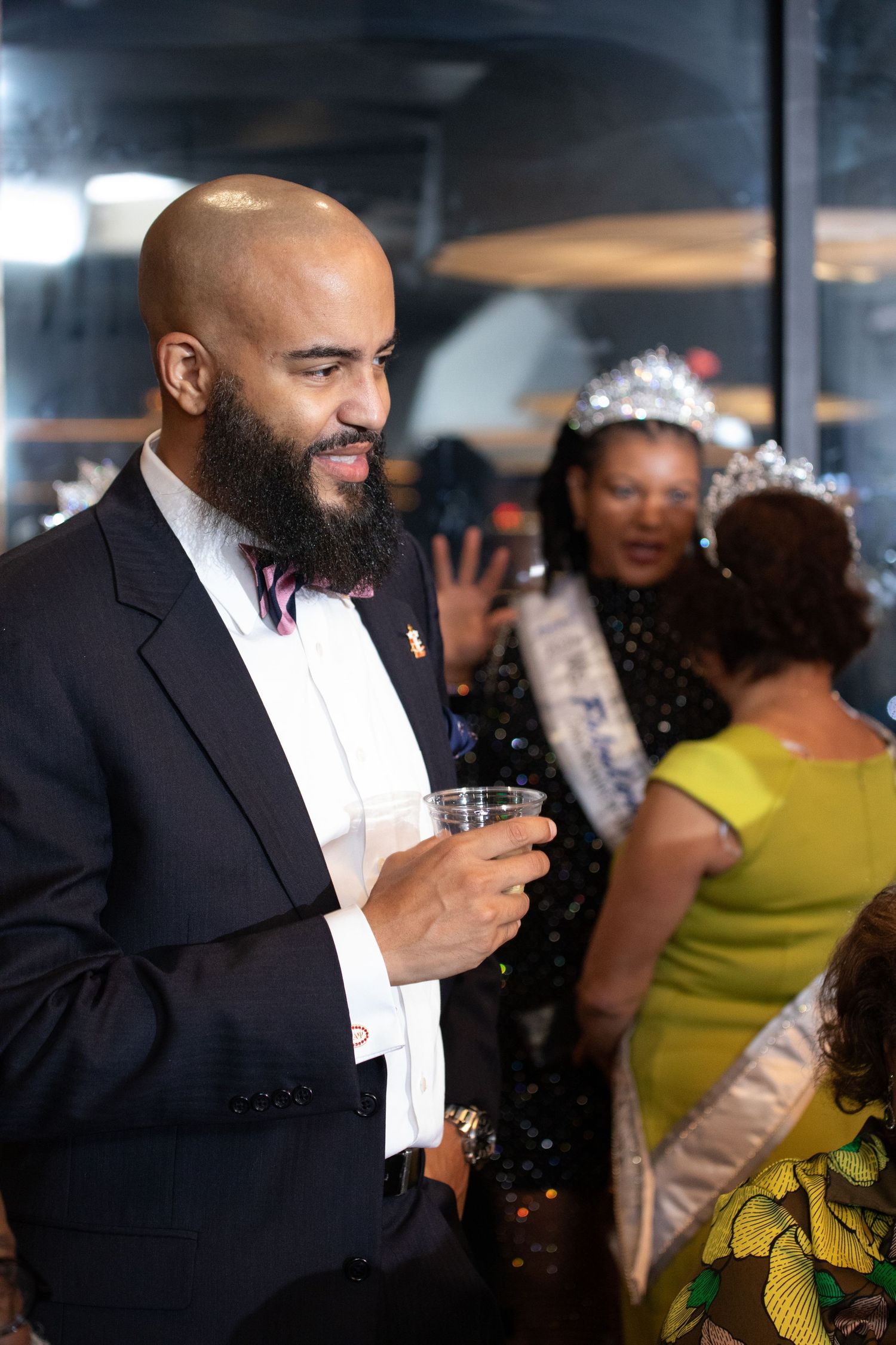 A well-dressed guest with a full beard enjoys a drink at an elegant social gathering.
