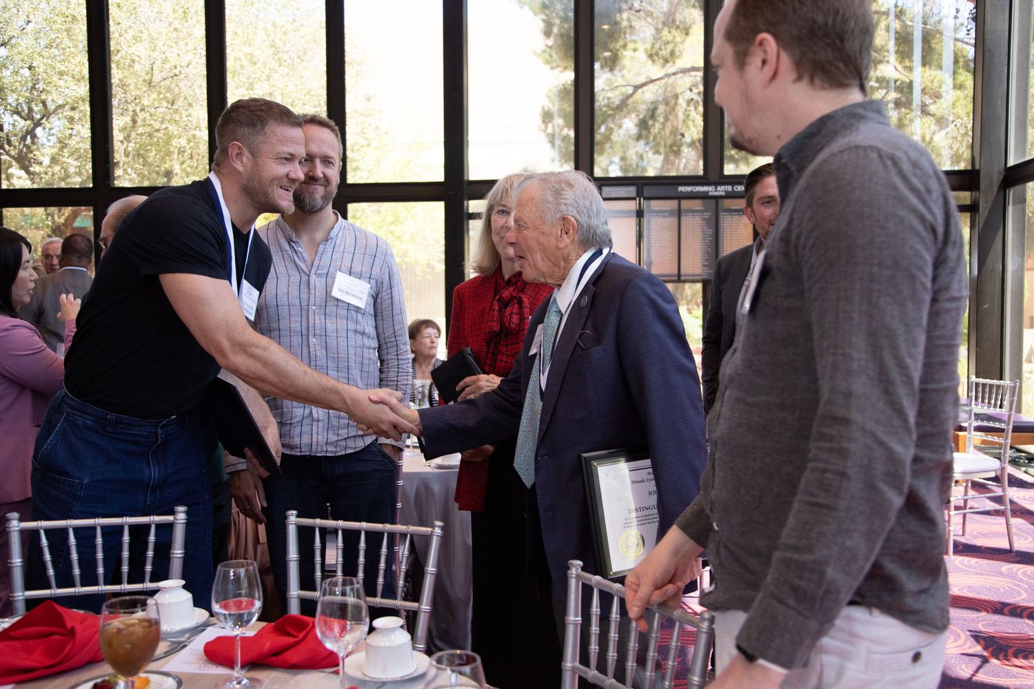 Group of people networking and shaking hands at formal event with table settings.