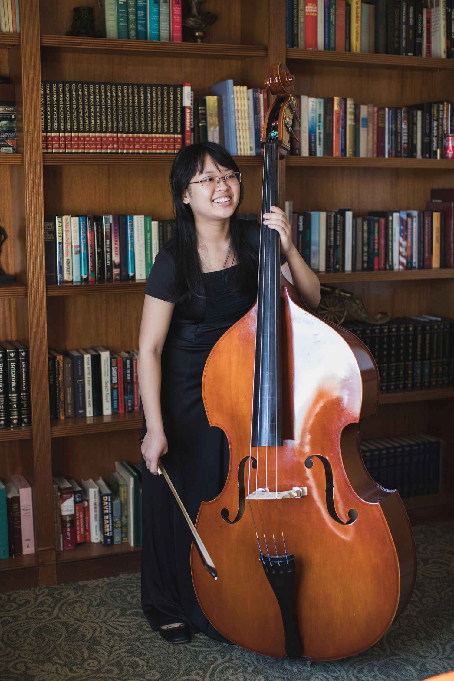 Double bass player smiles while posing with instrument in library setting.