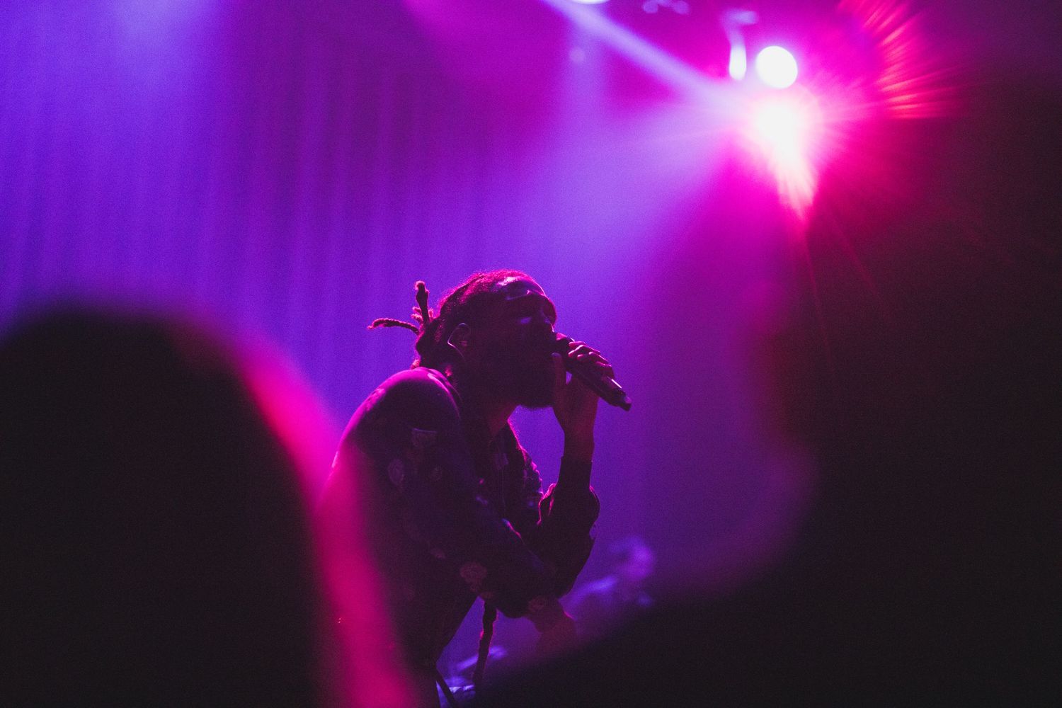 Silhouette of performer on stage against vibrant pink and purple concert lighting.