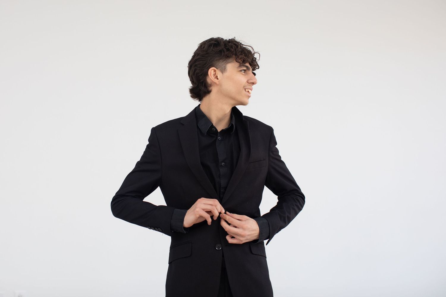Performer adjusts black suit jacket while posing against white background.