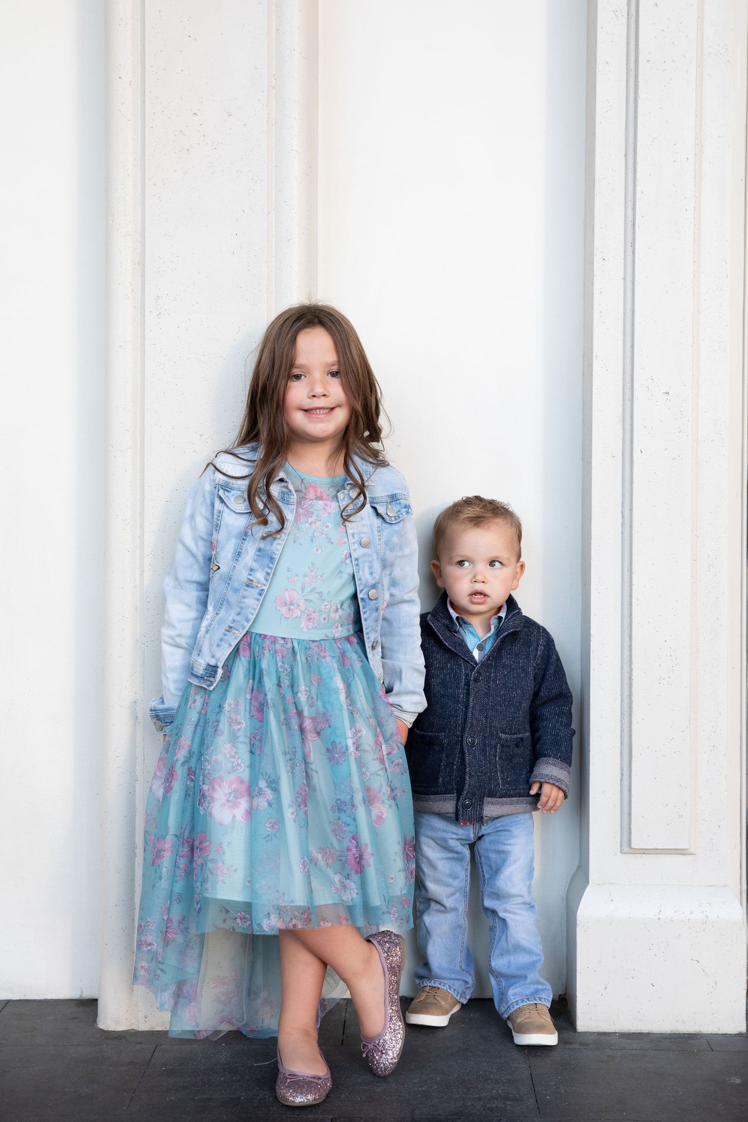 Two children pose against white columns wearing coordinating blue outfits.