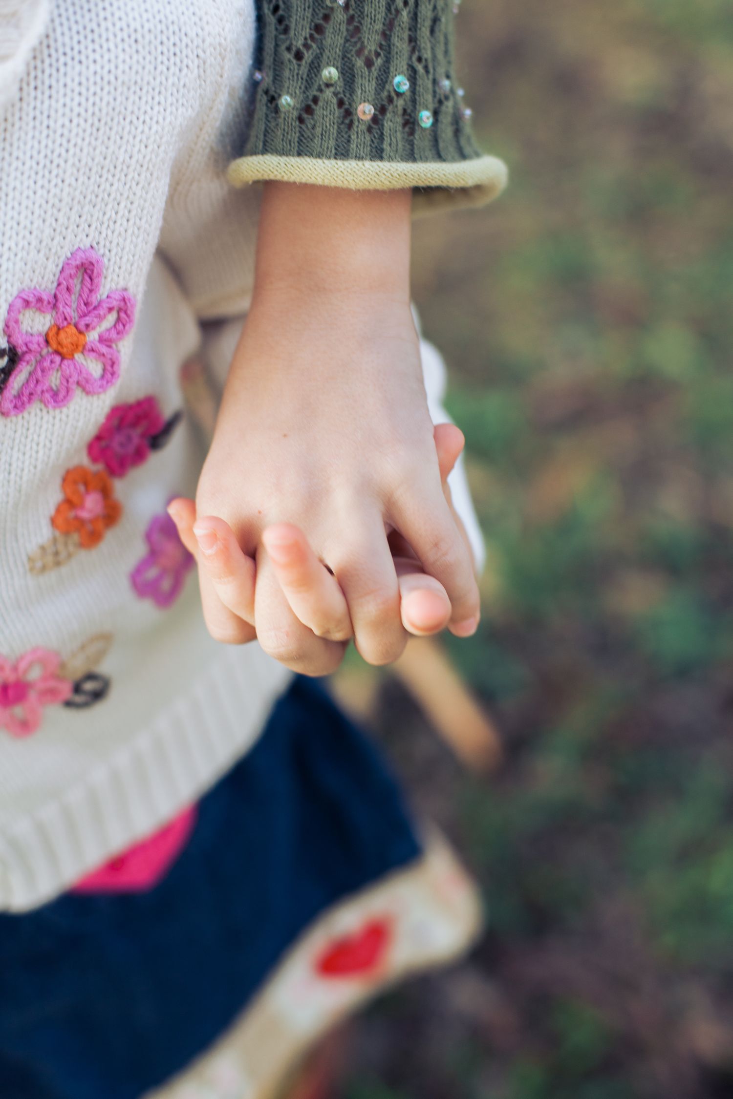 Close-up of two hands holding each other wearing embroidered floral sweater.
