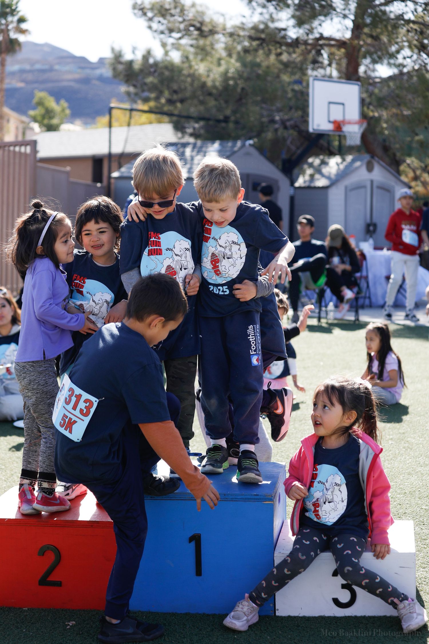 Children and adults celebrate on numbered podium steps during an outdoor event.