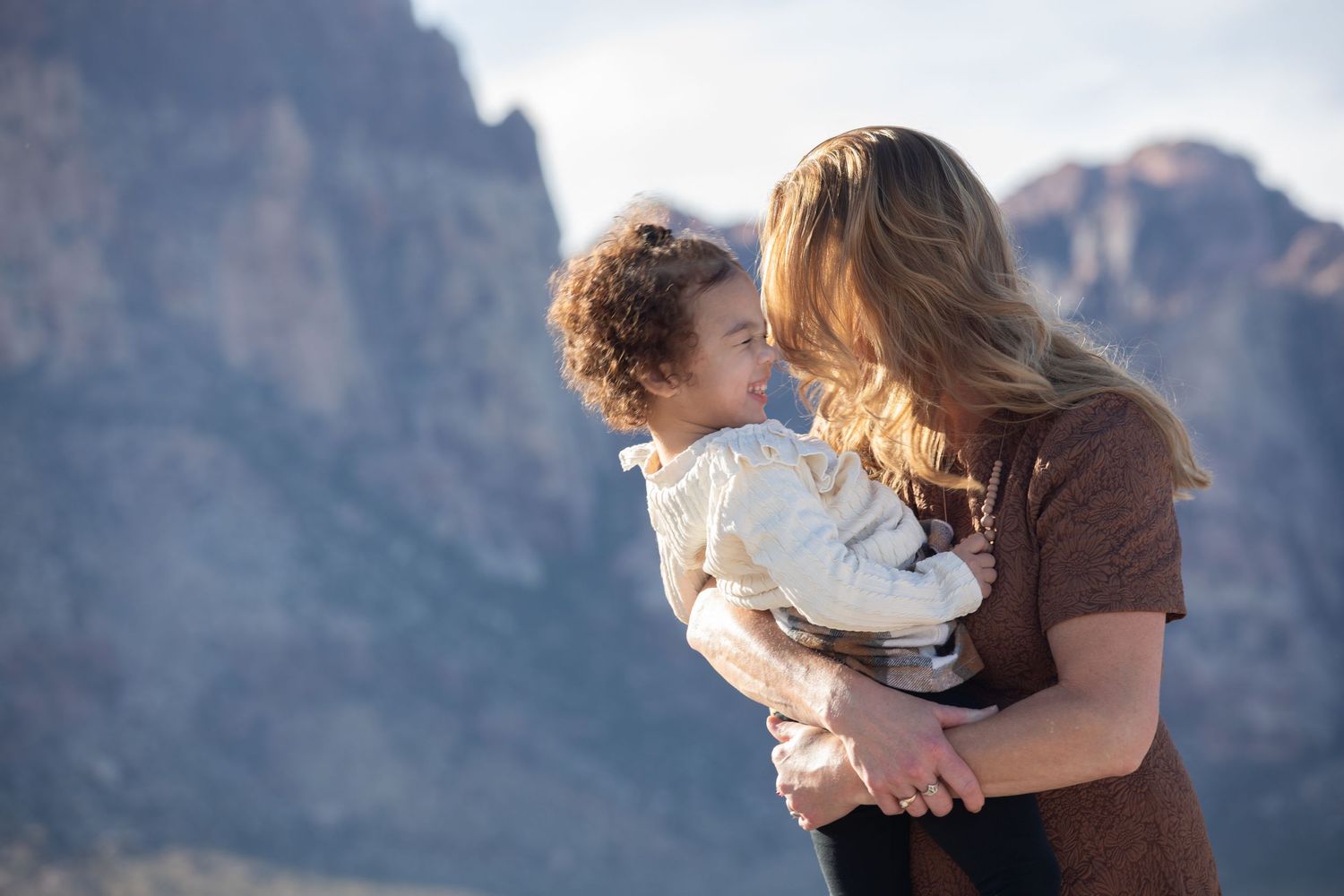 Parent and child share a tender moment against dramatic mountain scenery.