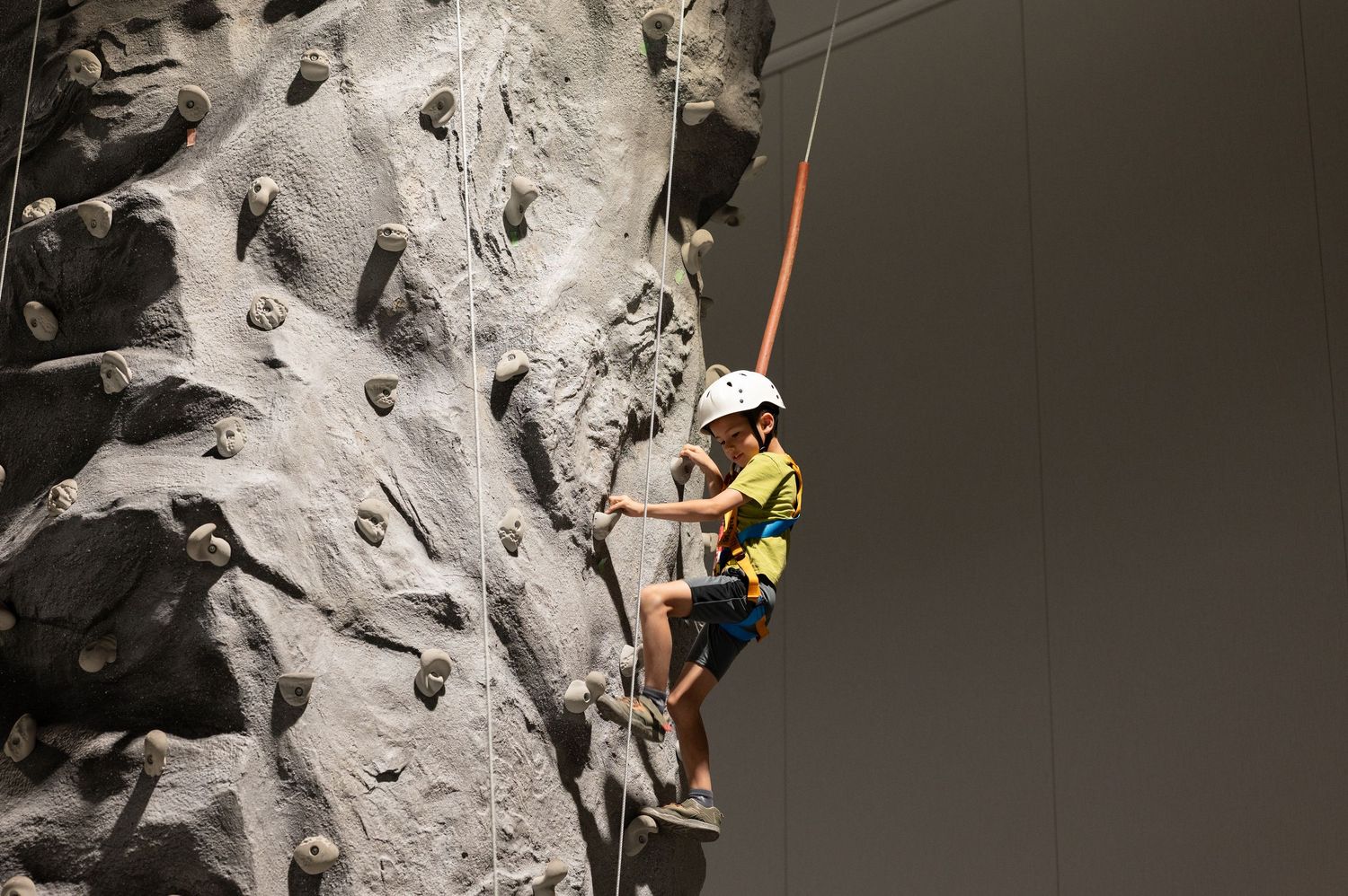 Person in safety gear climbing an indoor rock climbing wall with spotlights.