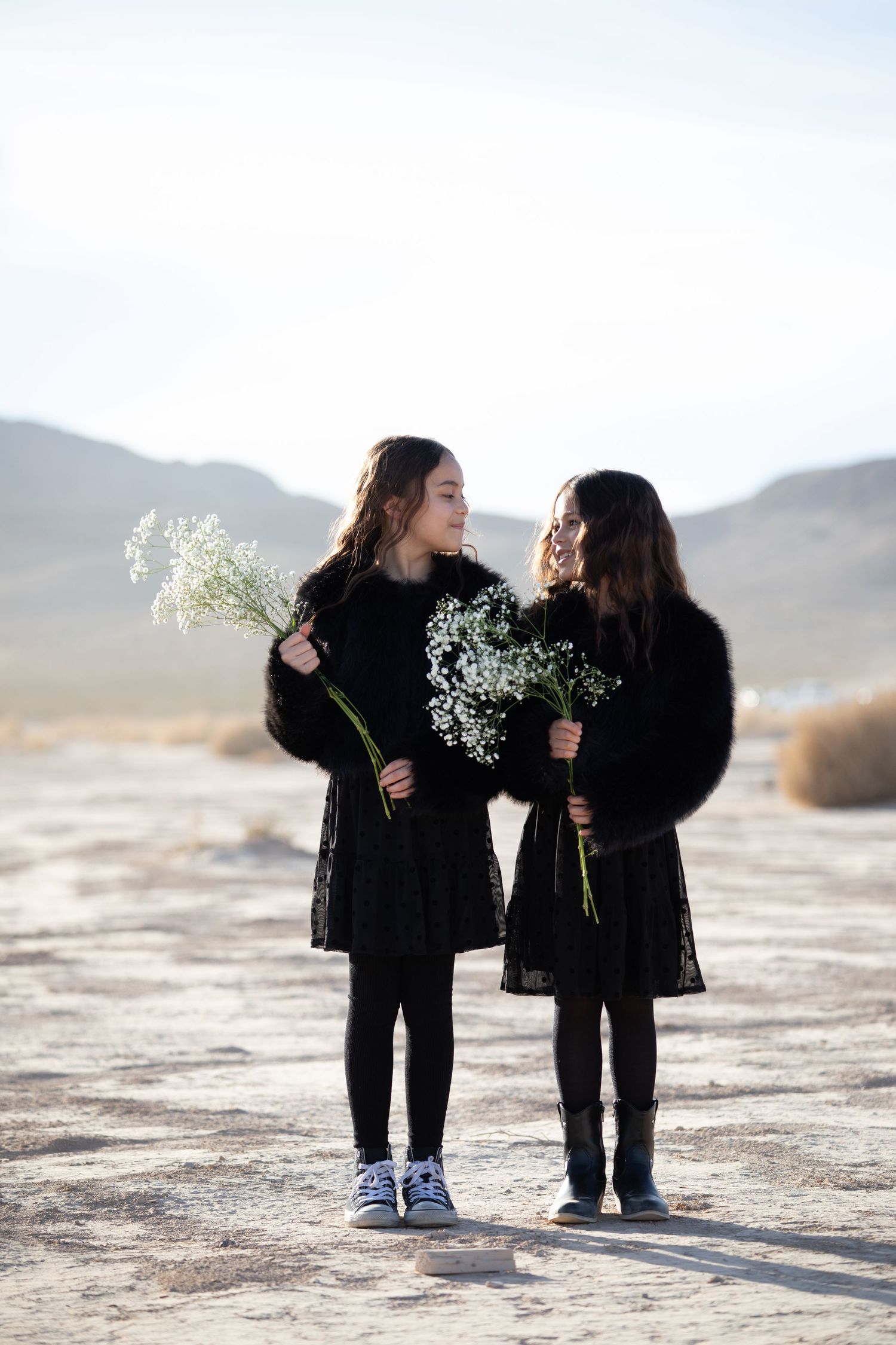 Two small children in black outfits holding baby's breath flowers in a desert setting.