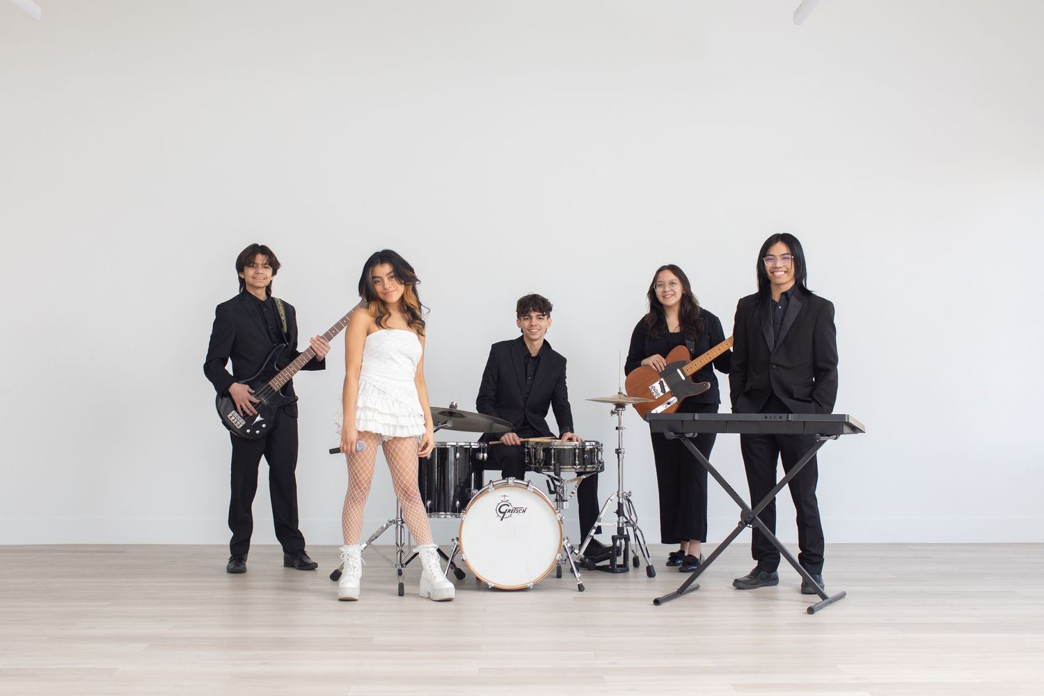 Musicians and performers resting against a white wall in casual attire.