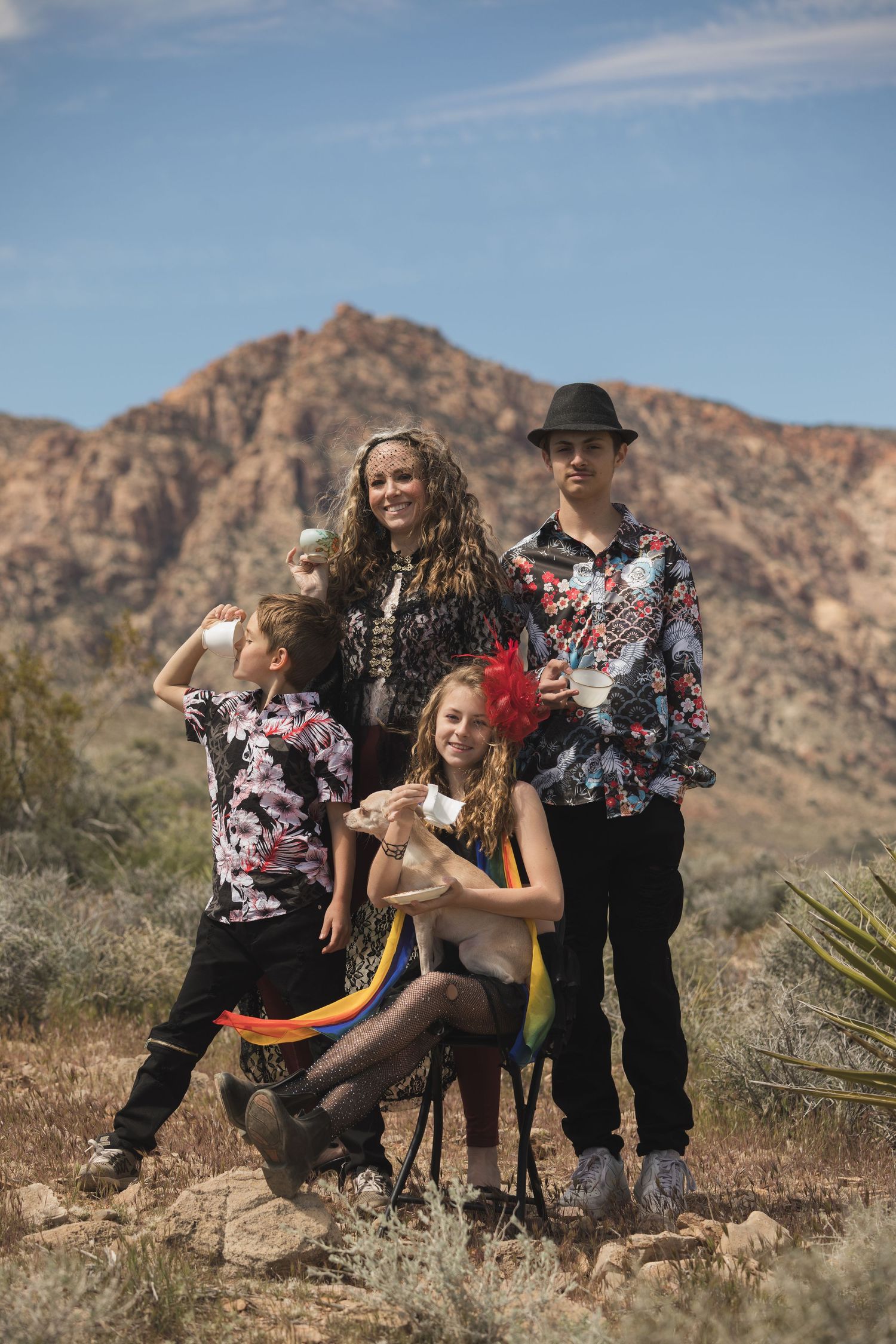 Group portrait in desert setting with matching tie-dye outfits against mountain backdrop.