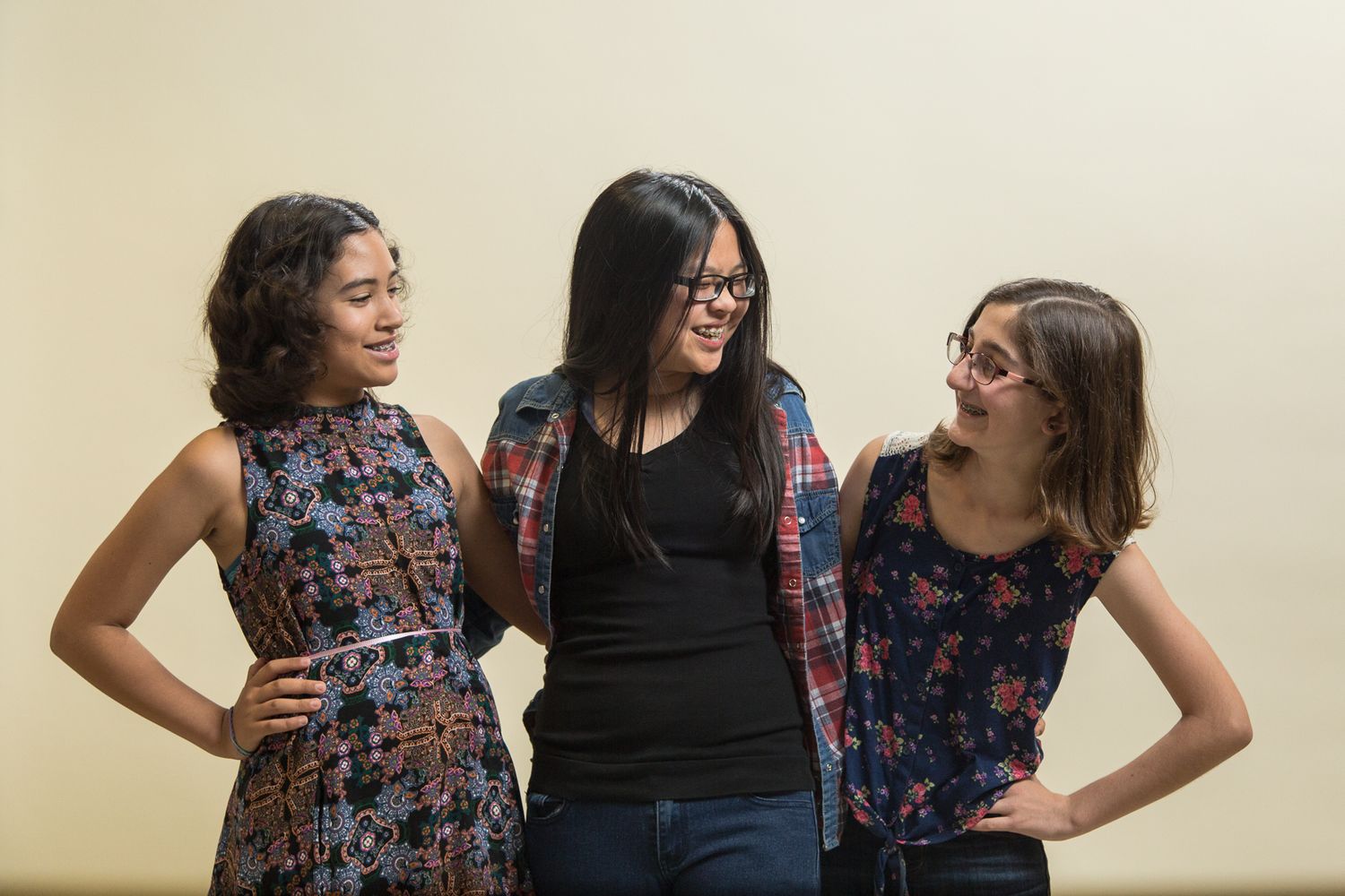 Three friends pose playfully against neutral wall.
