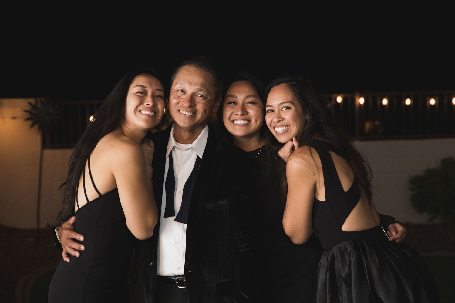 Group photo of formal-dressed people at evening event with string lights.