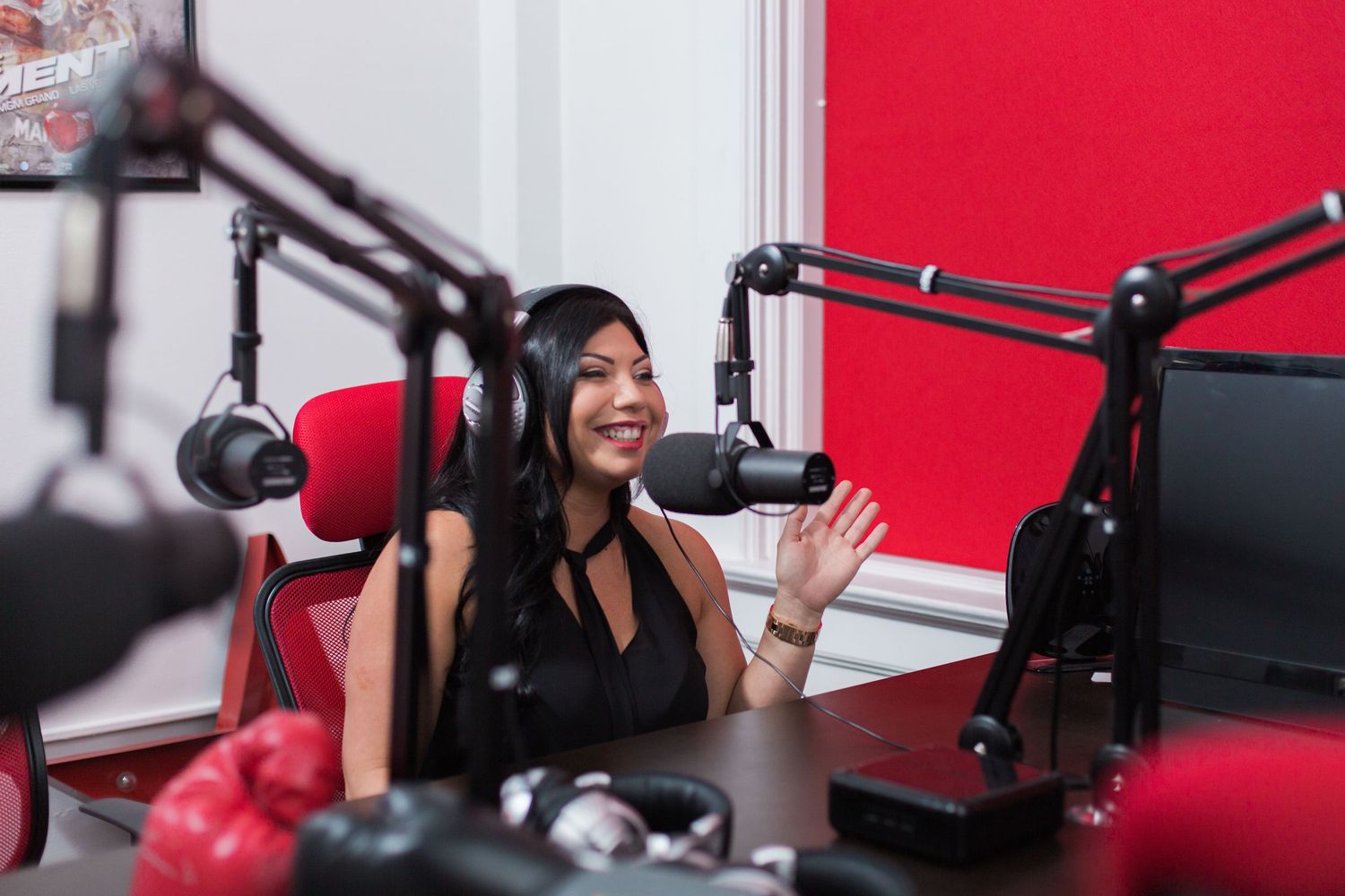 Radio host speaks into microphone in bright red studio setting with professional broadcast equipment.