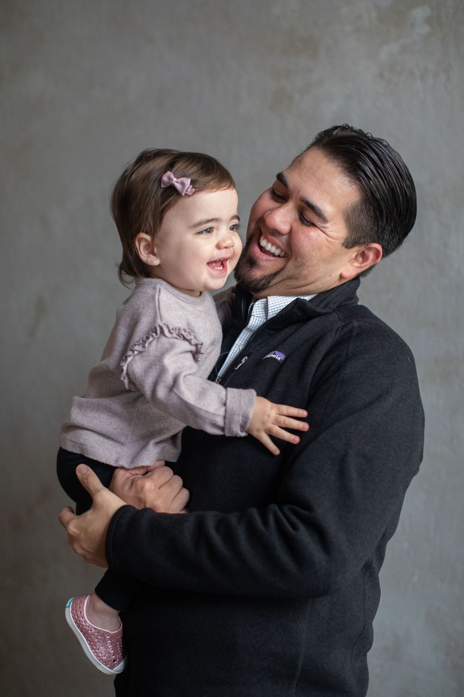 Parent and toddler sharing a happy moment together against gray background.