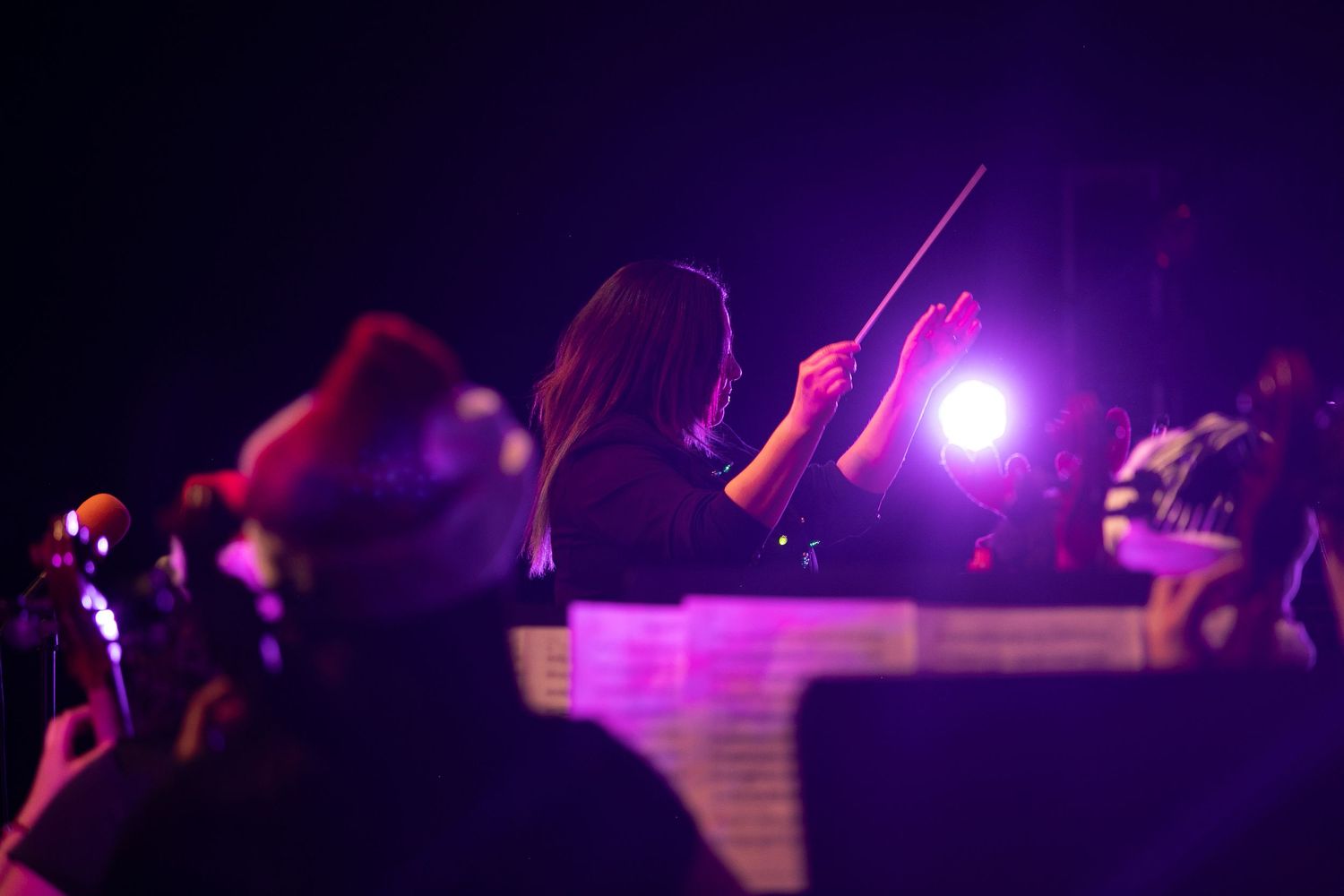 Orchestra conductor silhouetted against purple stage lights during performance.