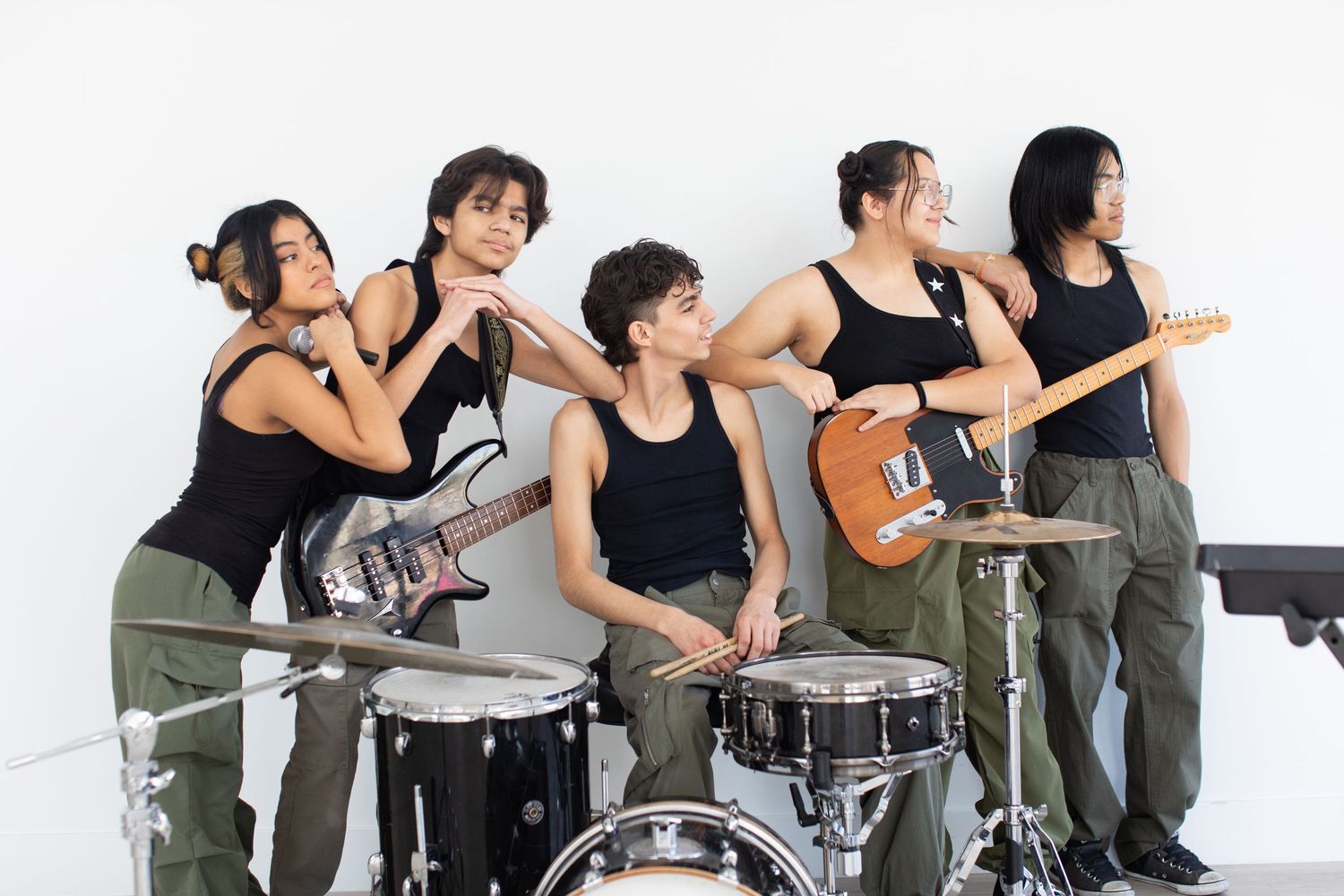Band members pose with their instruments including drums and guitars against white backdrop.