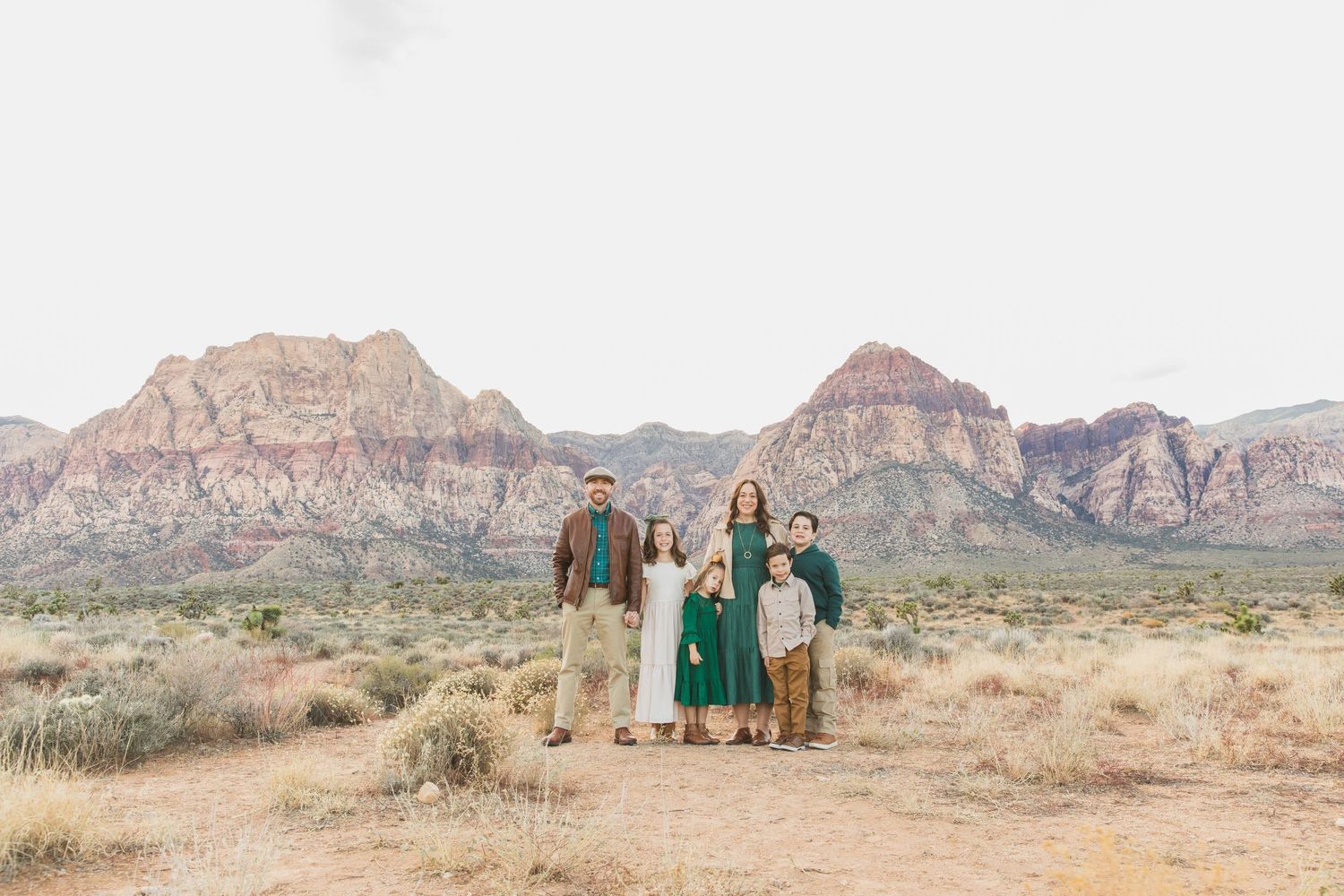 Family portrait with desert red rock mountains and scrubland in background.