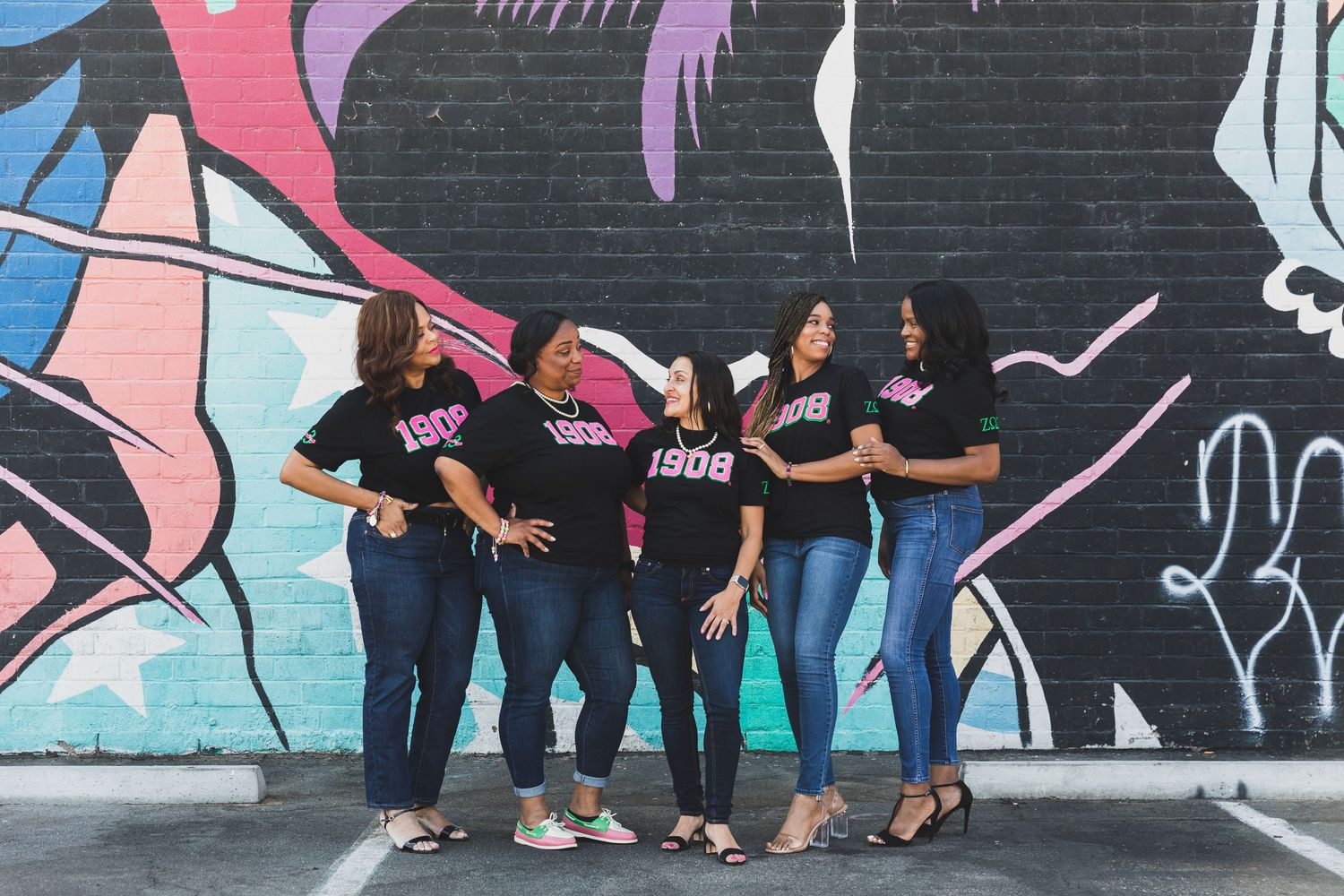 Group poses playfully in front of colorful street art mural.