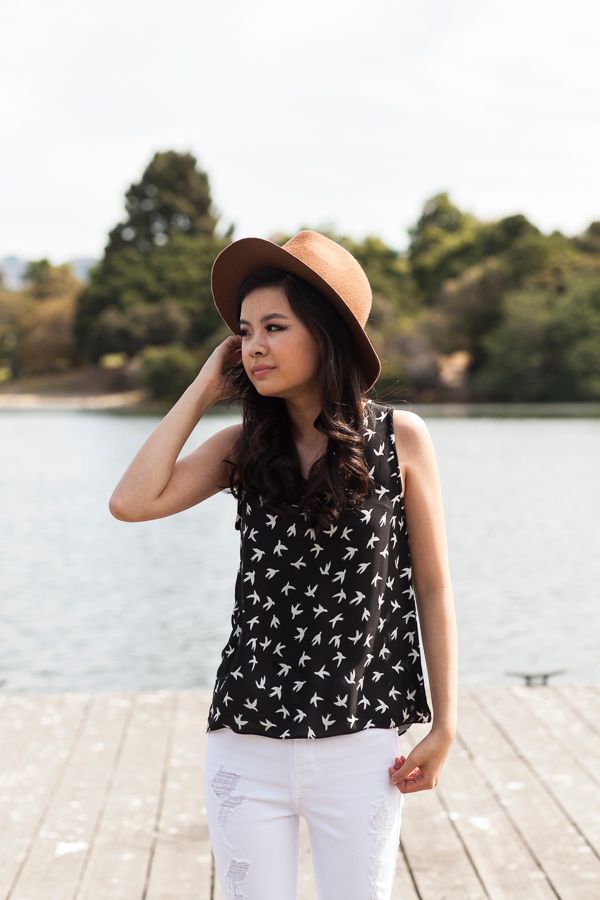 Stylish summer outfit with black patterned top and white pants photographed on wooden dock by the lake.