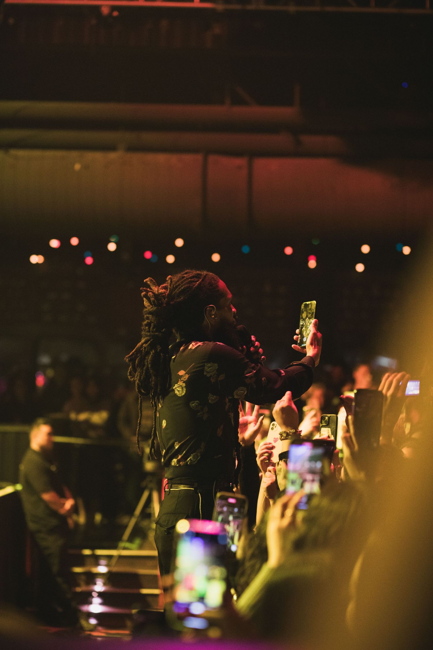 Concert performer engages with crowd while fans hold up phones with lights in dark venue.