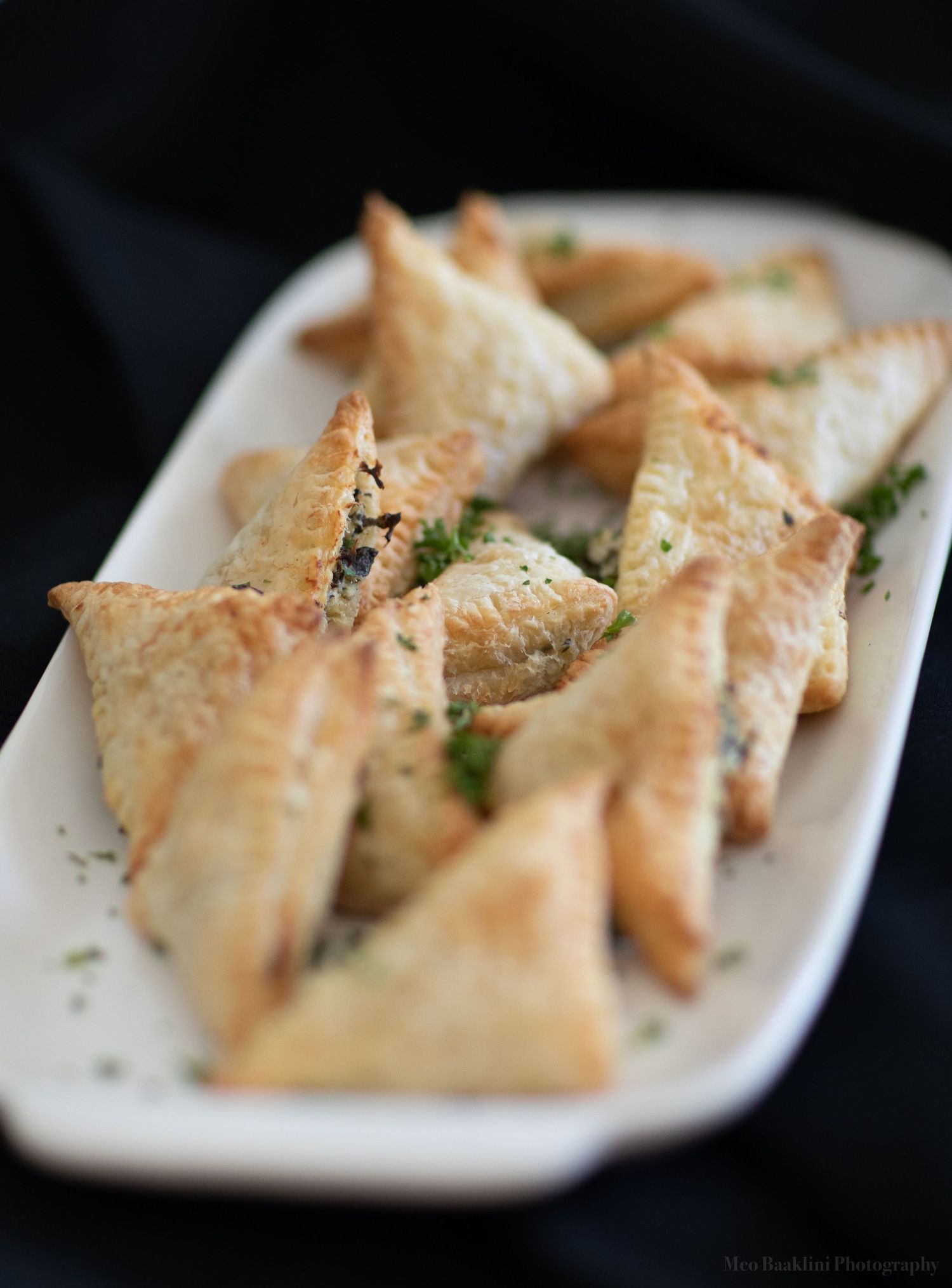 Golden phyllo pastries arranged on white serving plate with fresh herb garnish.