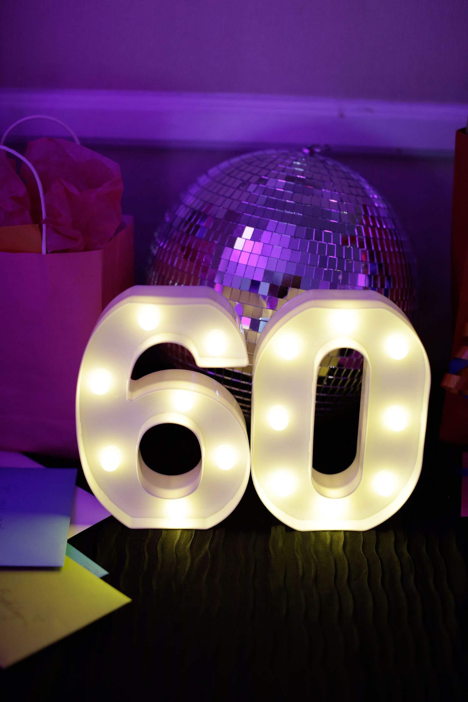Illuminated number 60 sign with disco ball in purple lighting.