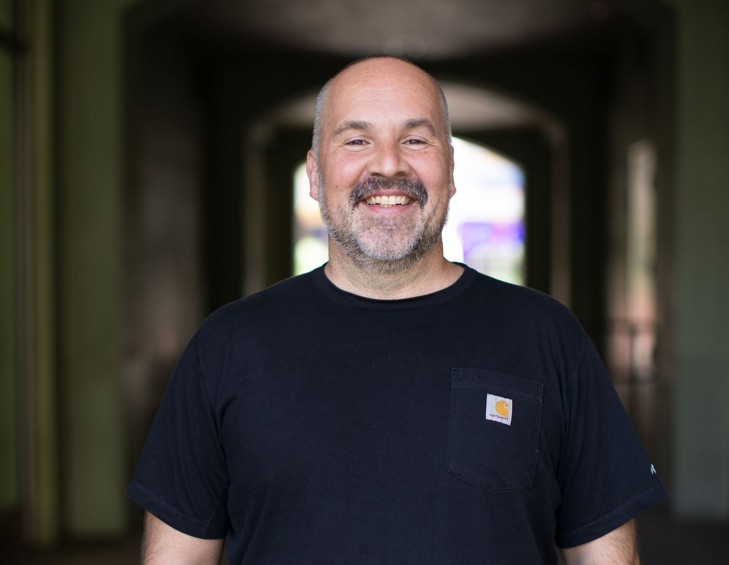 A casual portrait of someone wearing a black Carhartt t-shirt with a joyful smile in an indoor setting.