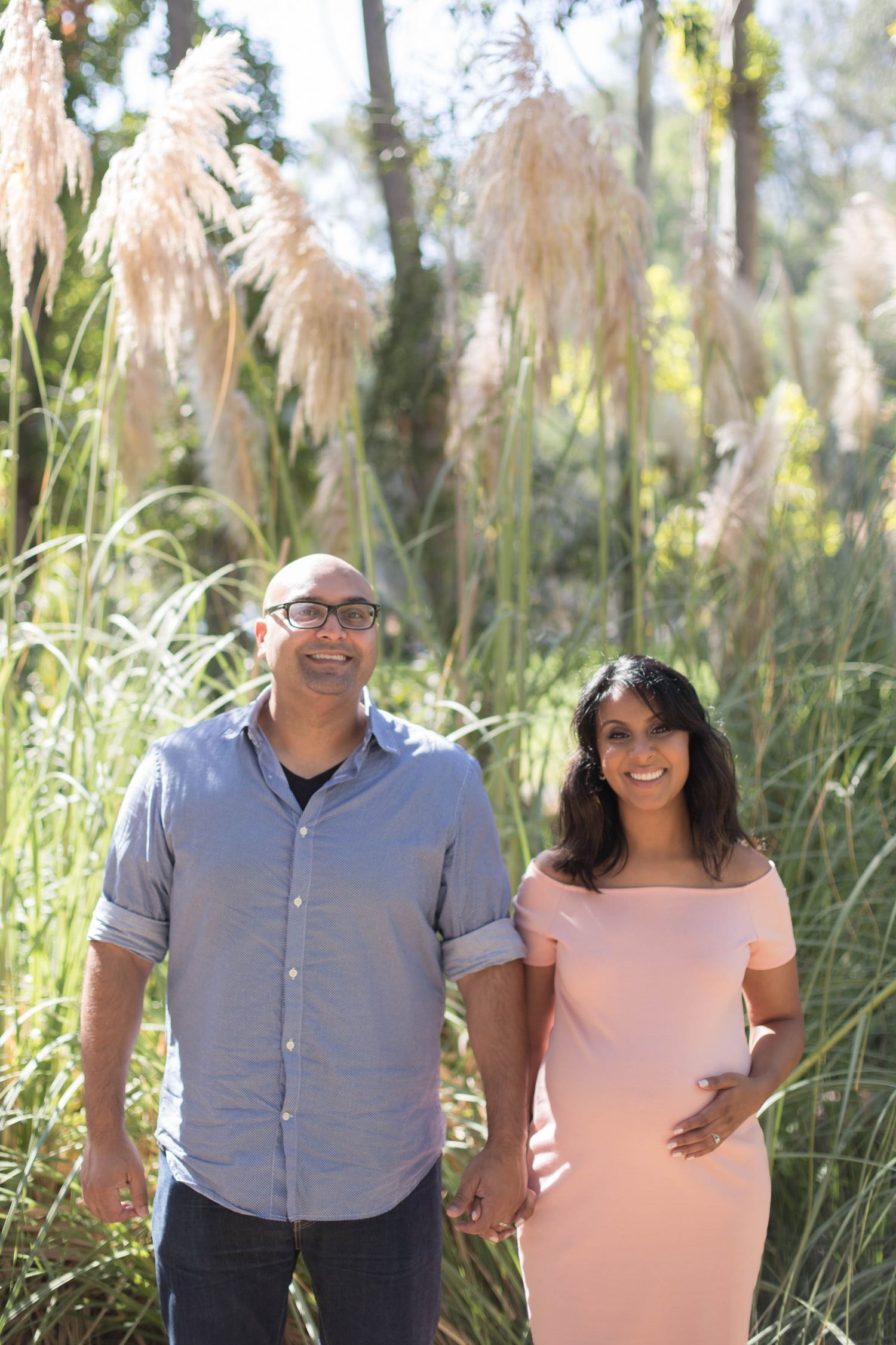 Couple holding hands in front of tall pampas grass during outdoor photo session.