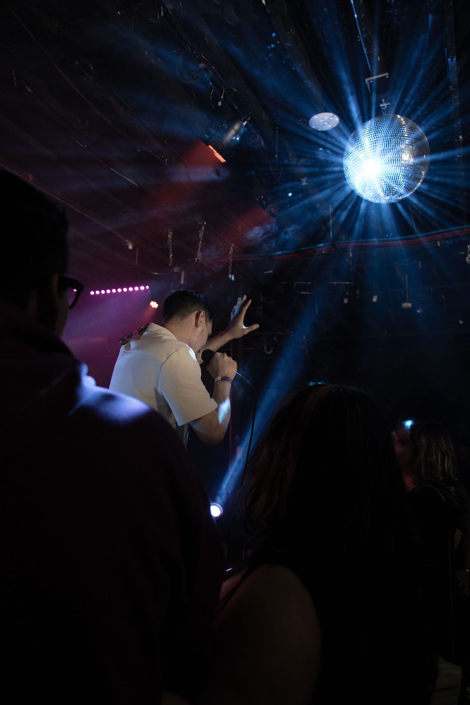A performer silhouetted against dramatic stage lighting with blue beams and a disco ball effect.