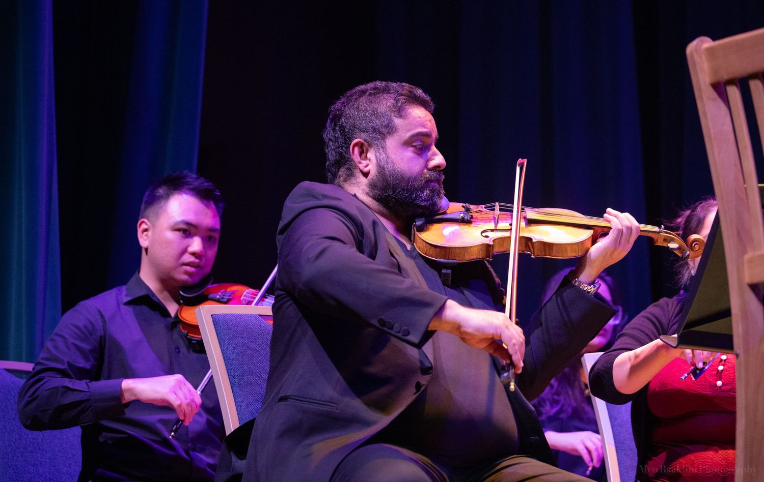 Musicians play violin and string instruments under theatrical stage lighting.
