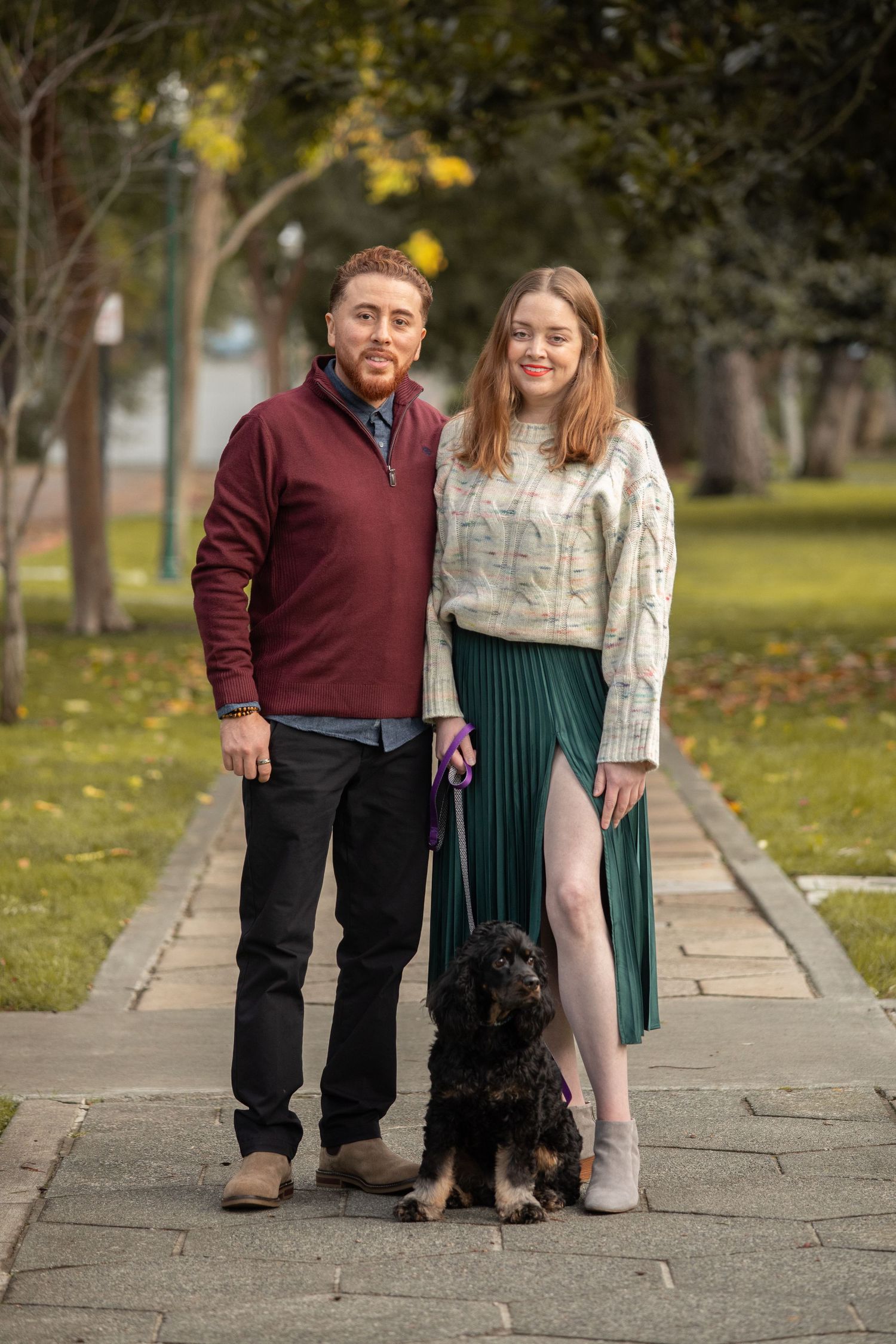 A couple and their black dog pose together on stone steps during an autumn photoshoot.
