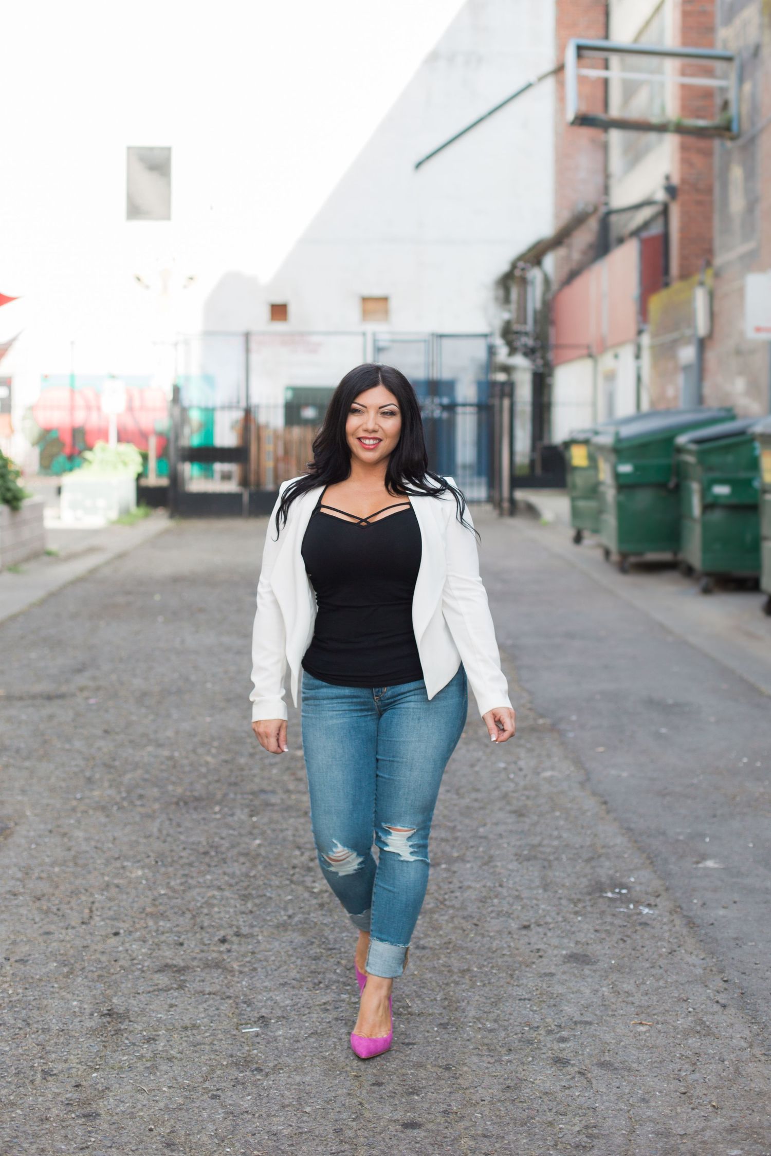 Stylish casual business attire with white blazer and pink heels walking down urban alley.